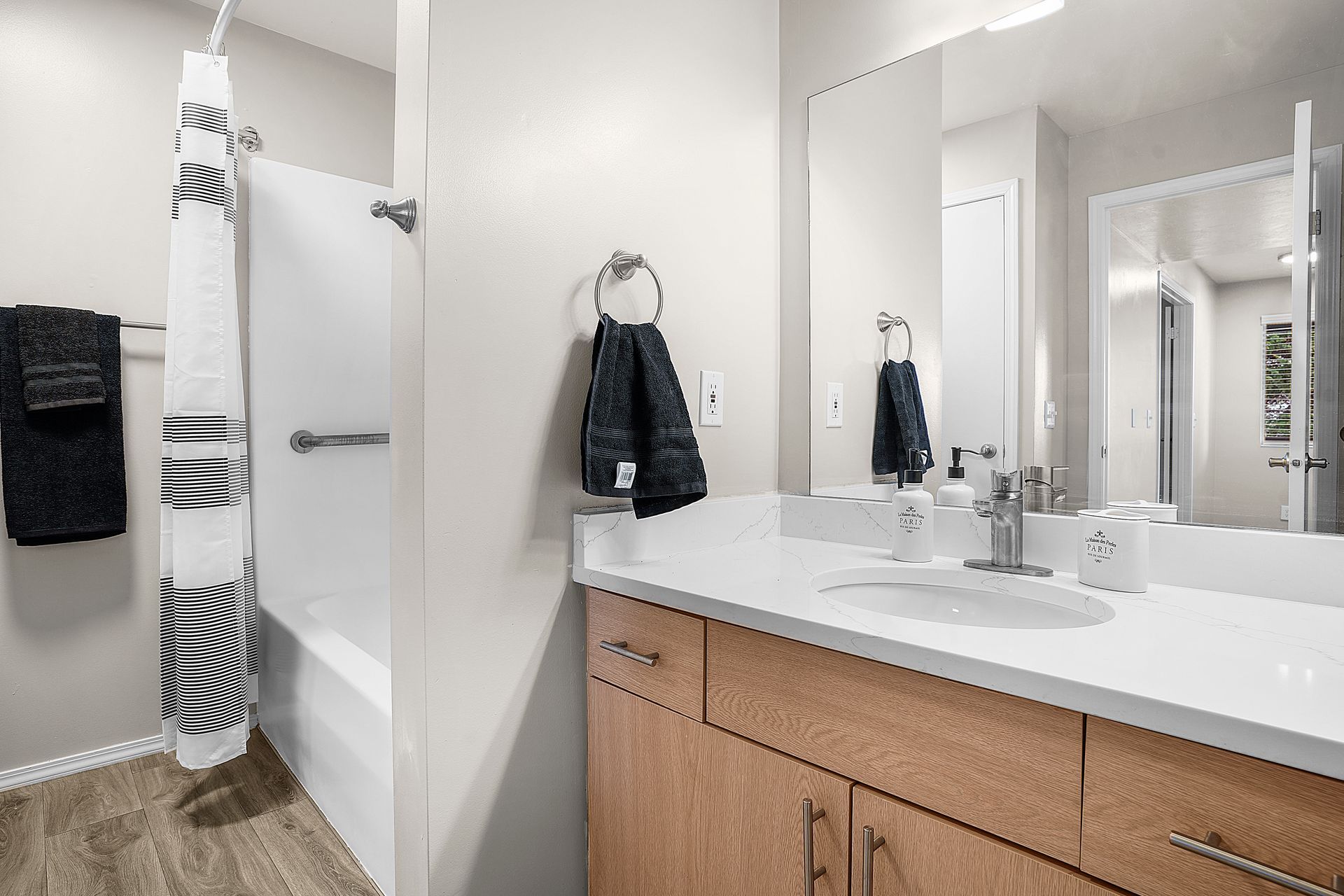 Bathroom with a tub and shower, sink, light wood cabinets, and large mirror. Black and white towels.