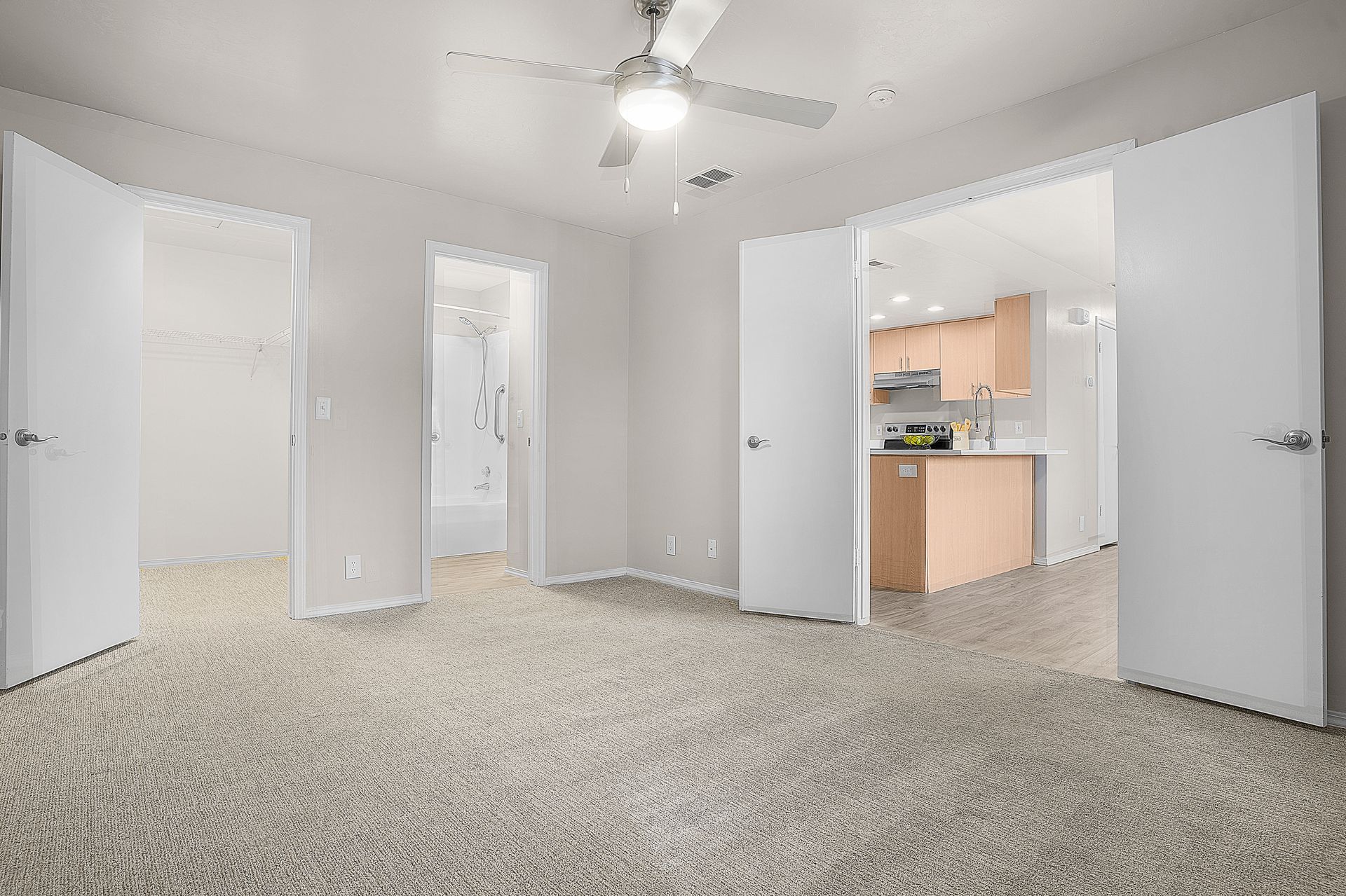Bedroom with carpet, open doors to closet, bathroom, and kitchen, neutral colors.