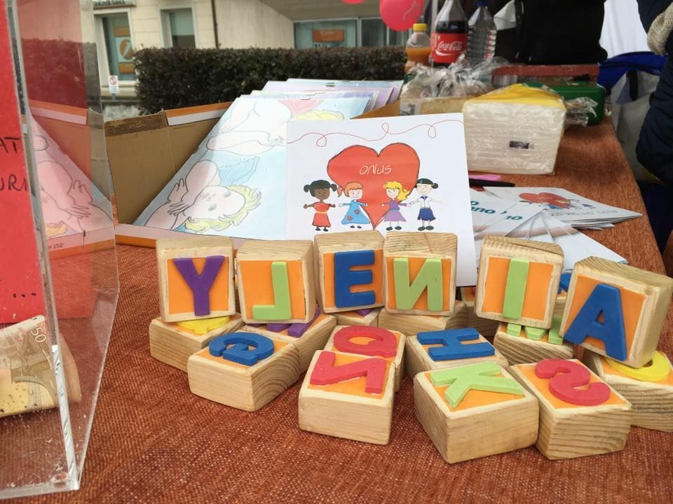 Blocchi di legno con lettere colorate disposti in un'esposizione accanto a un disegno di bambini in piedi davanti a un cuore rosso.
