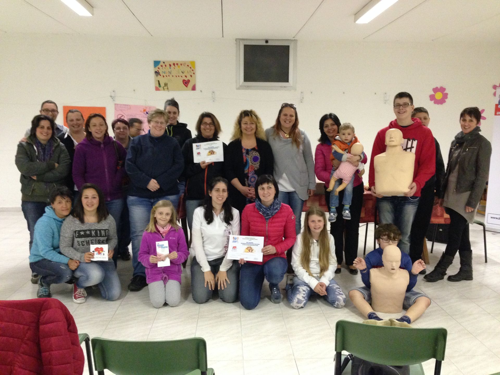 Un gruppo di persone si riunisce in una stanza luminosa durante una sessione di addestramento al primo soccorso e alla rianimazione cardiopolmonare (RCP) con l'ausilio di manichini medici.