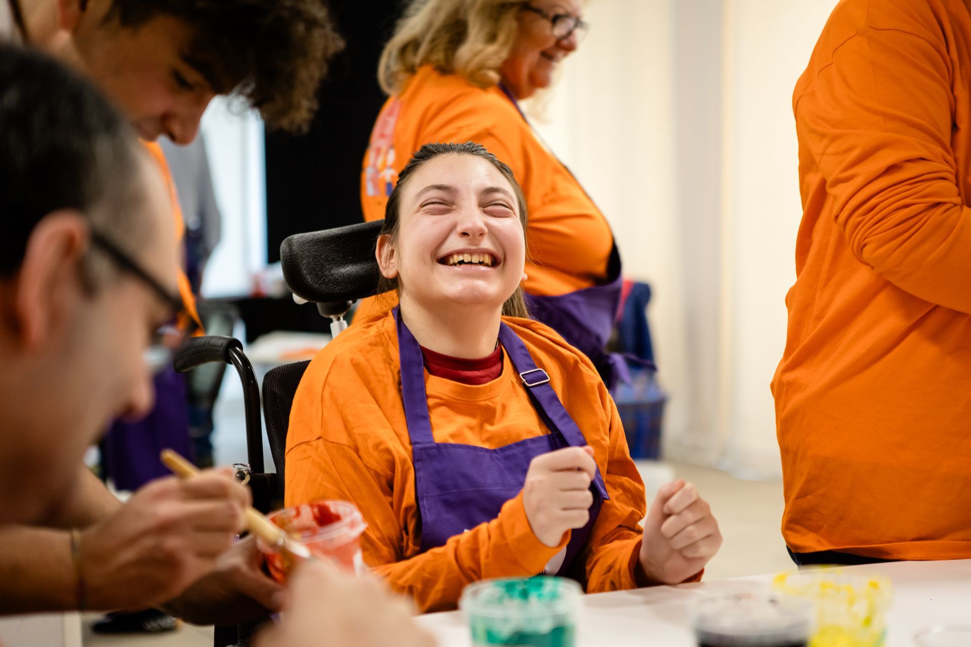 Un gruppo di persone che indossano magliette arancioni e grembiuli viola abbinati si dedica allegramente a un'attività di pittura attorno a un tavolo.