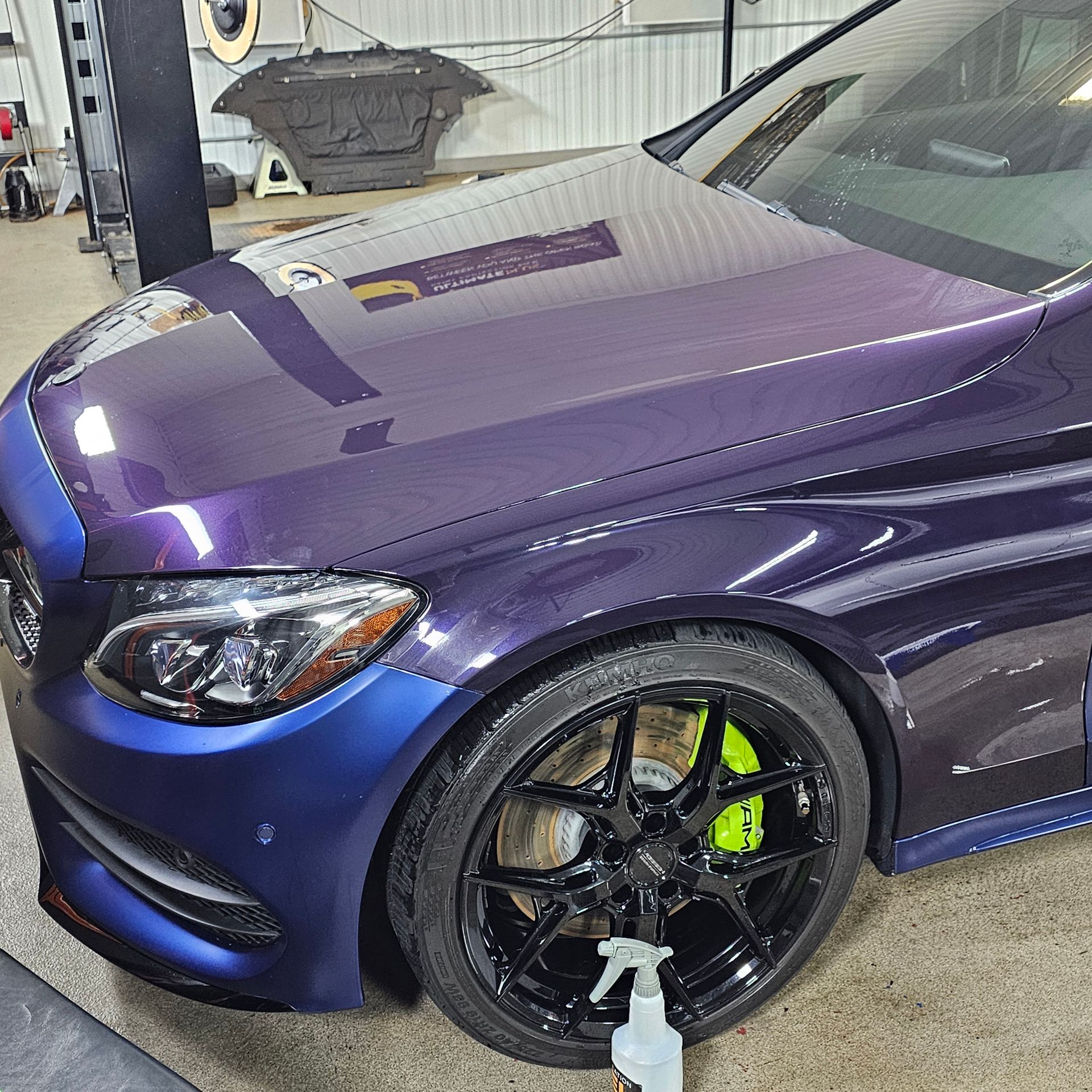 Dark purple Mercedes-Benz sedan with custom wheels and lime green brake calipers in a garage.