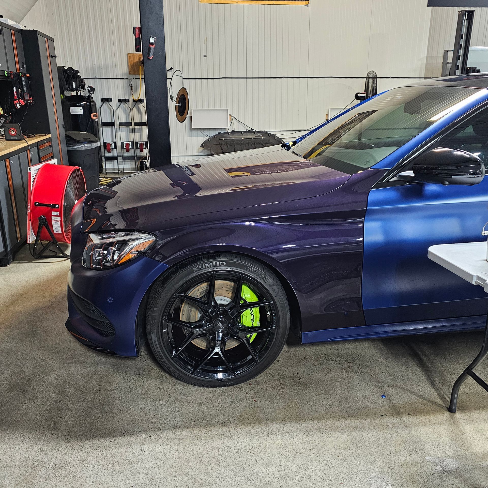 Blue car in a garage with black rims, green brake calipers, and a two-tone paint job.