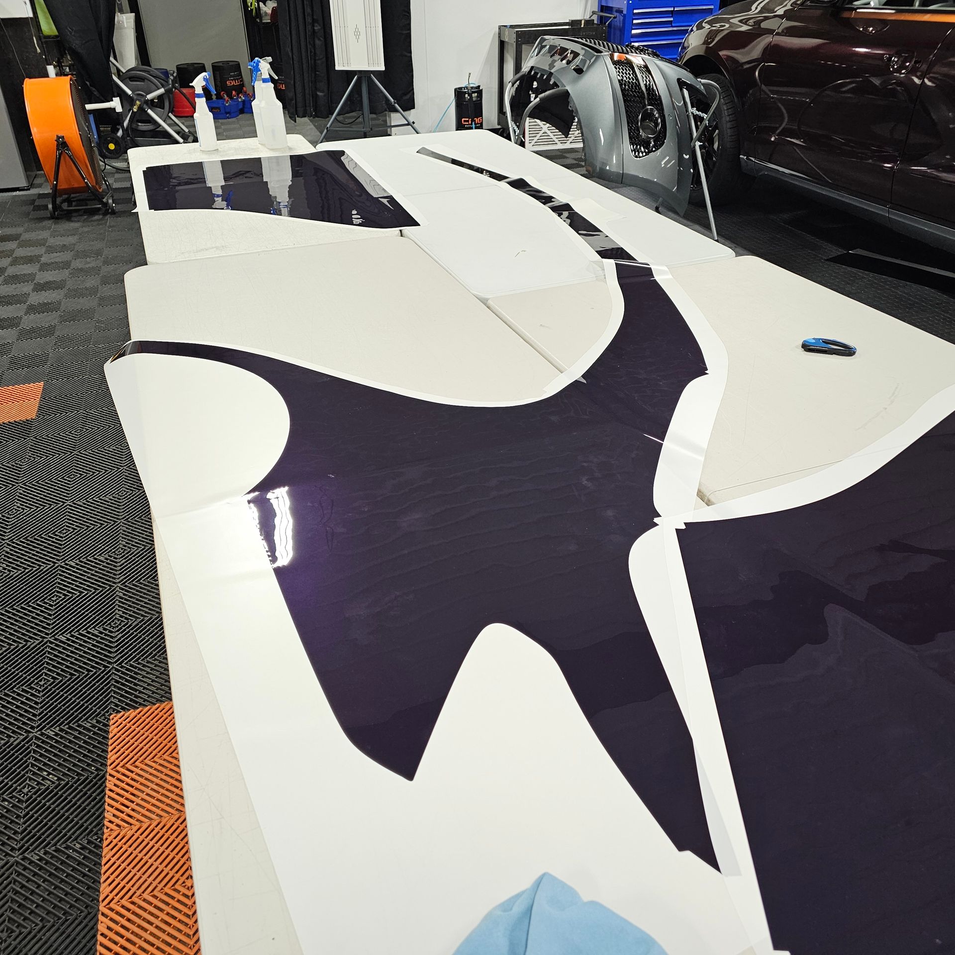 Purple vinyl car wrap pieces laid on a white table in a workshop.