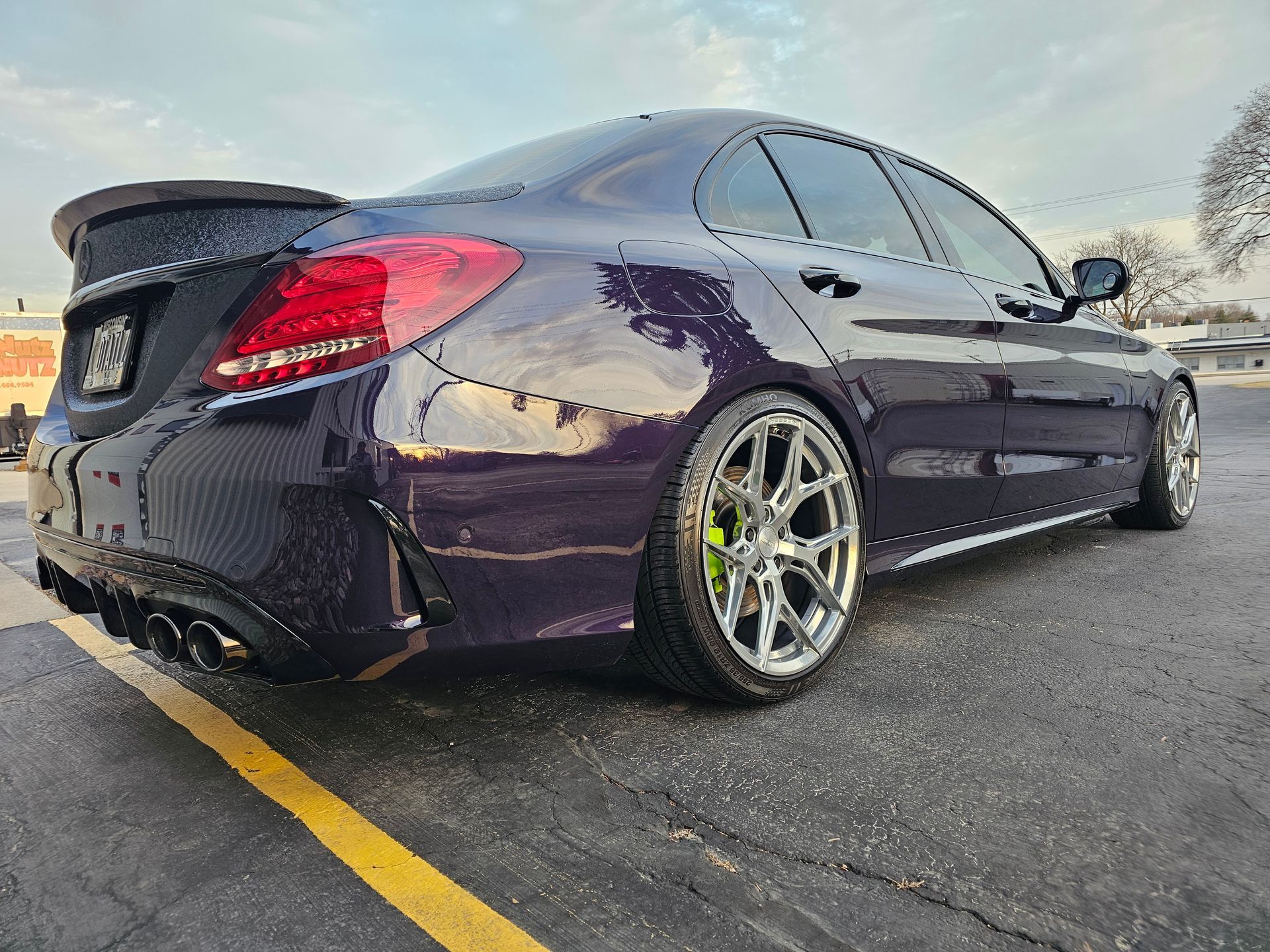 Purple Mercedes sedan with chrome wheels, black spoiler, and bright taillights on asphalt.