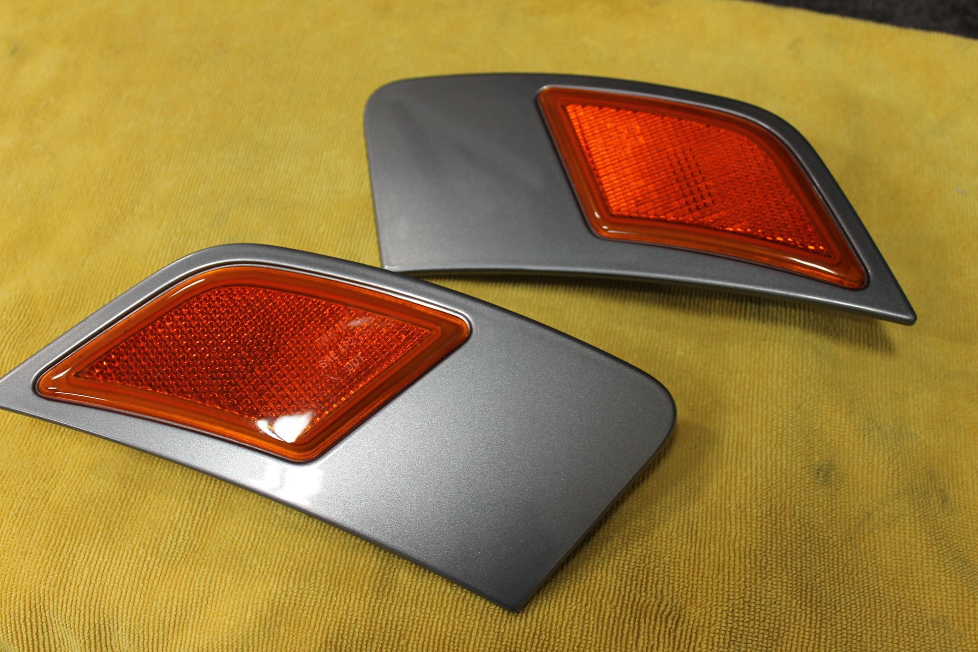 Two gray car side markers with orange reflectors, on a yellow surface.