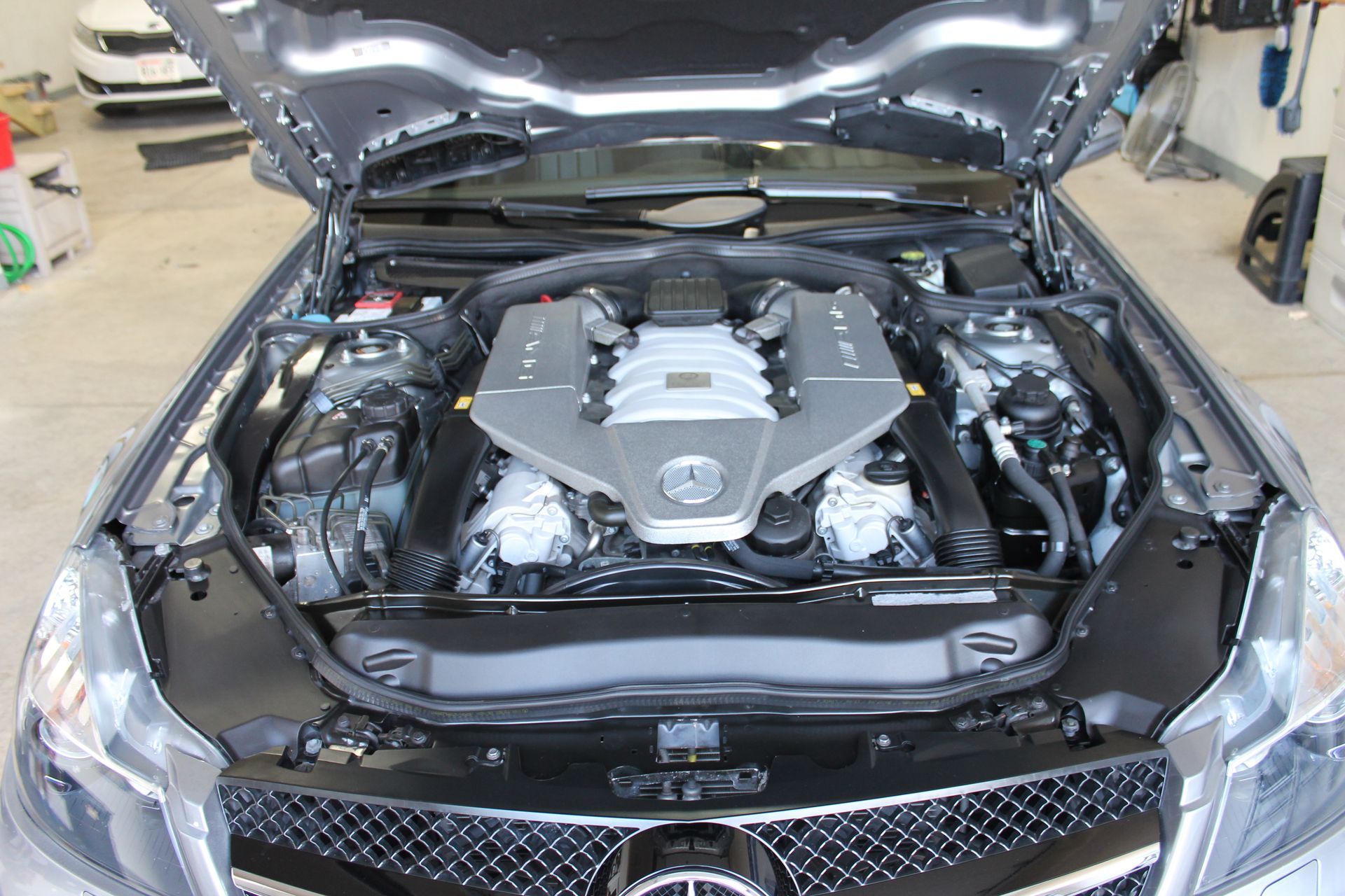 Mercedes-Benz engine under the hood of a car. Silver engine block and surrounding components are visible.
