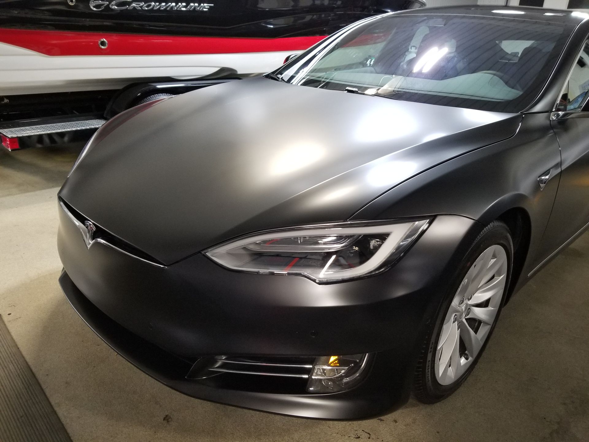 Matte gray Tesla parked, with boat in background.