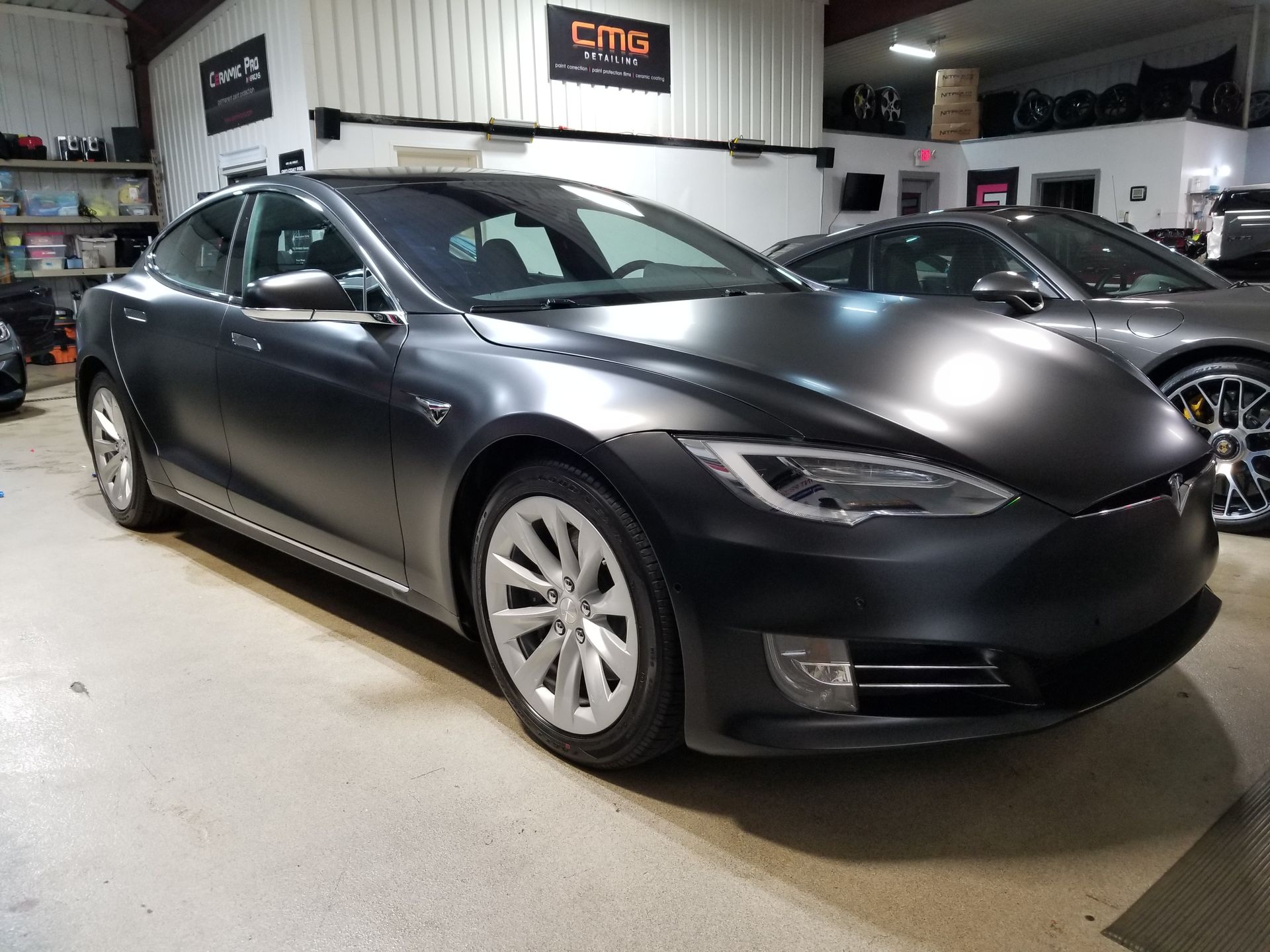 Dark gray Tesla sedan in a shop, matte finish.