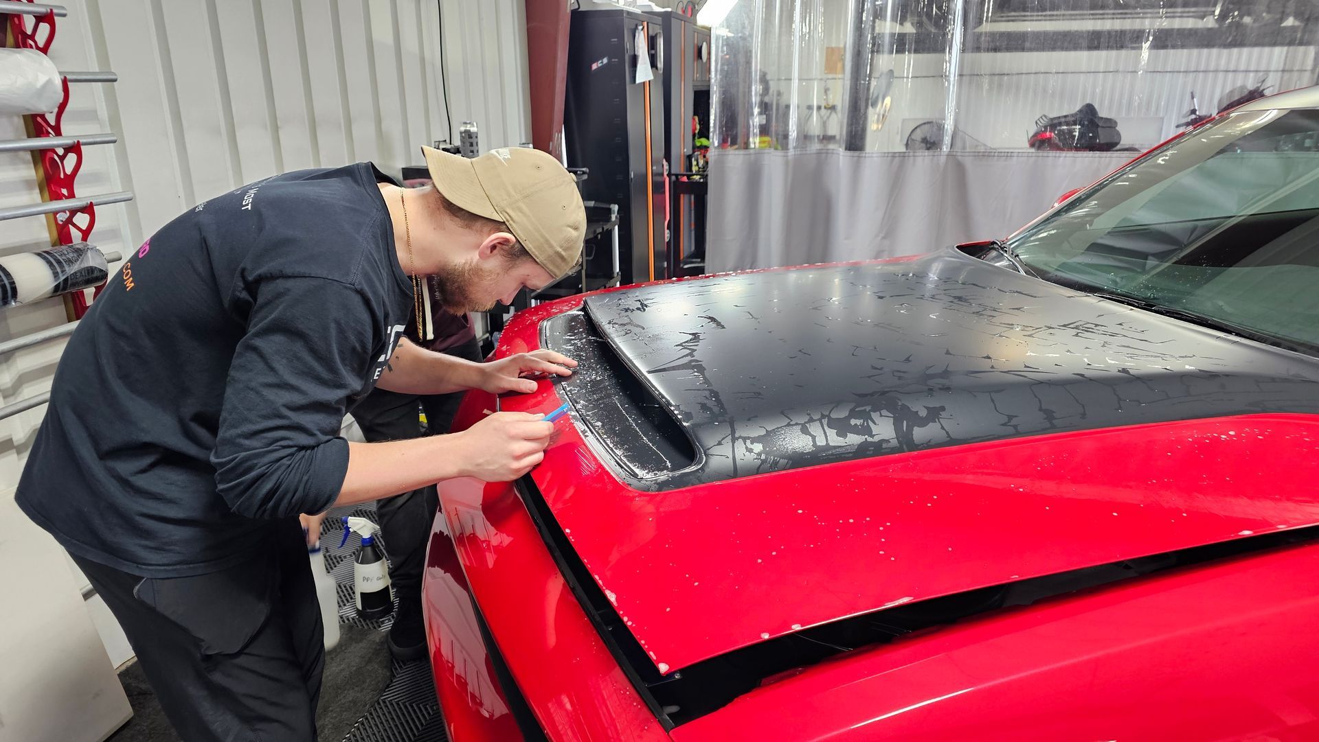 Two people applying a black wrap to a red car roof in a shop.