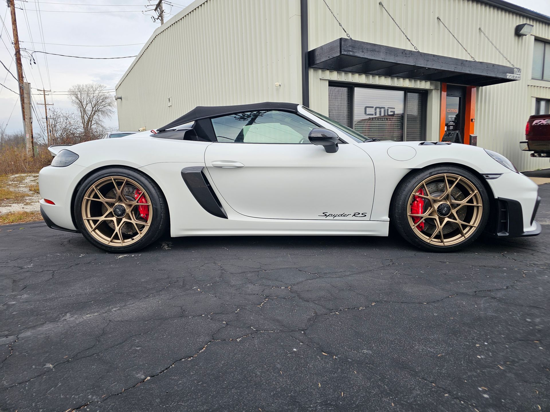 White Porsche convertible with bronze rims and red brake calipers parked outside a building.