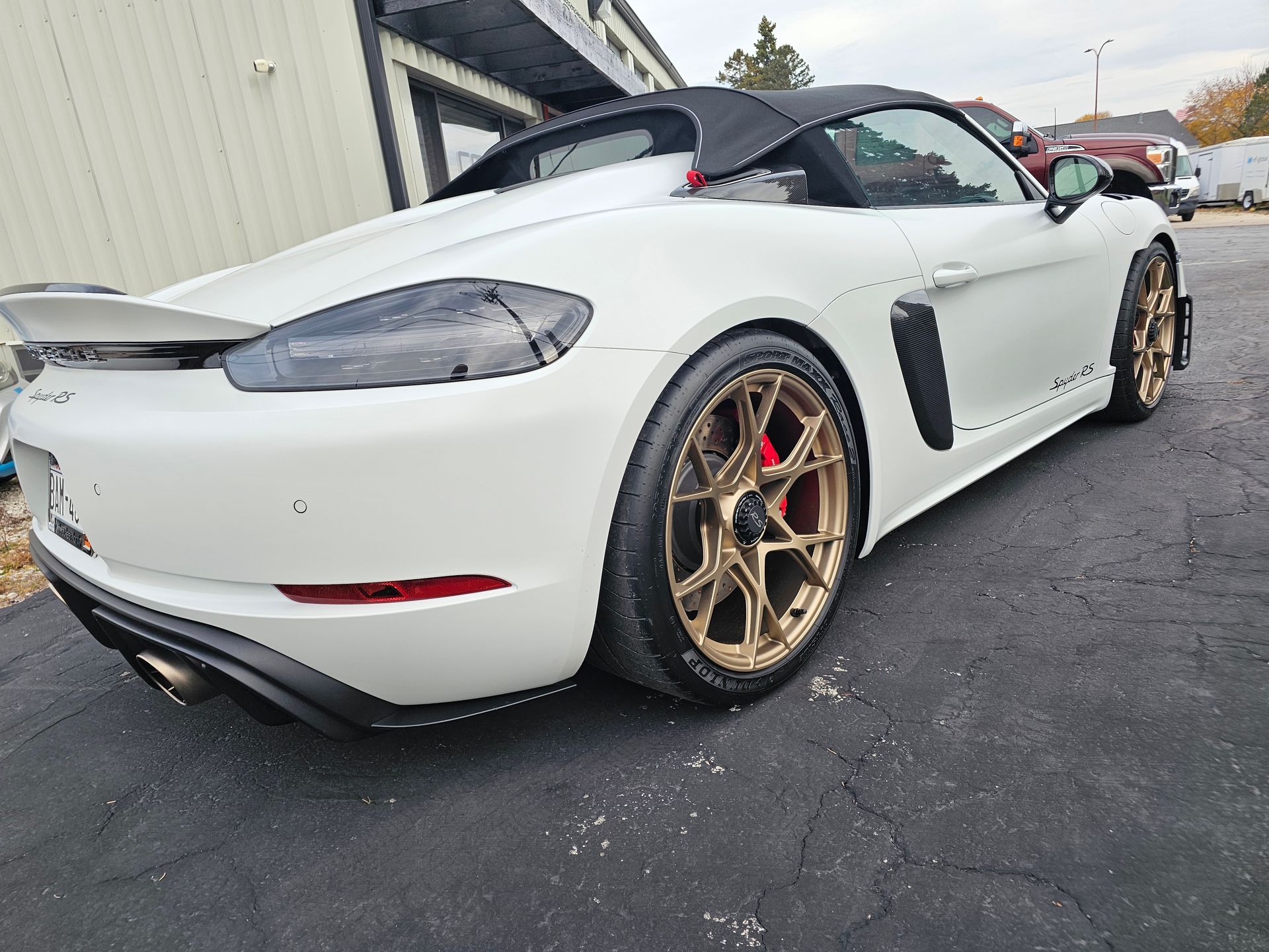 White Porsche convertible with bronze wheels on asphalt.