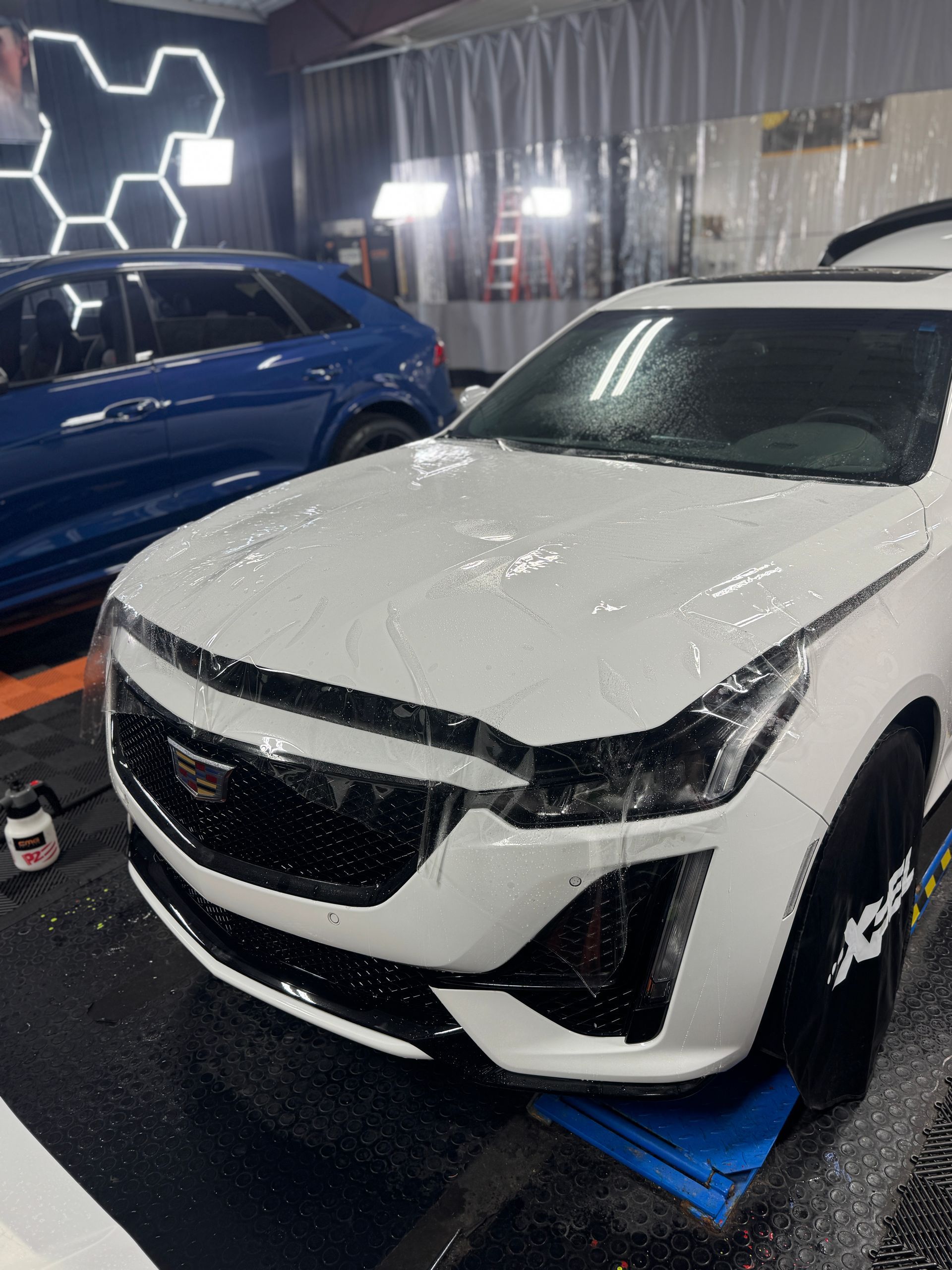 White Cadillac being washed in a detailing shop, blue car in the background.