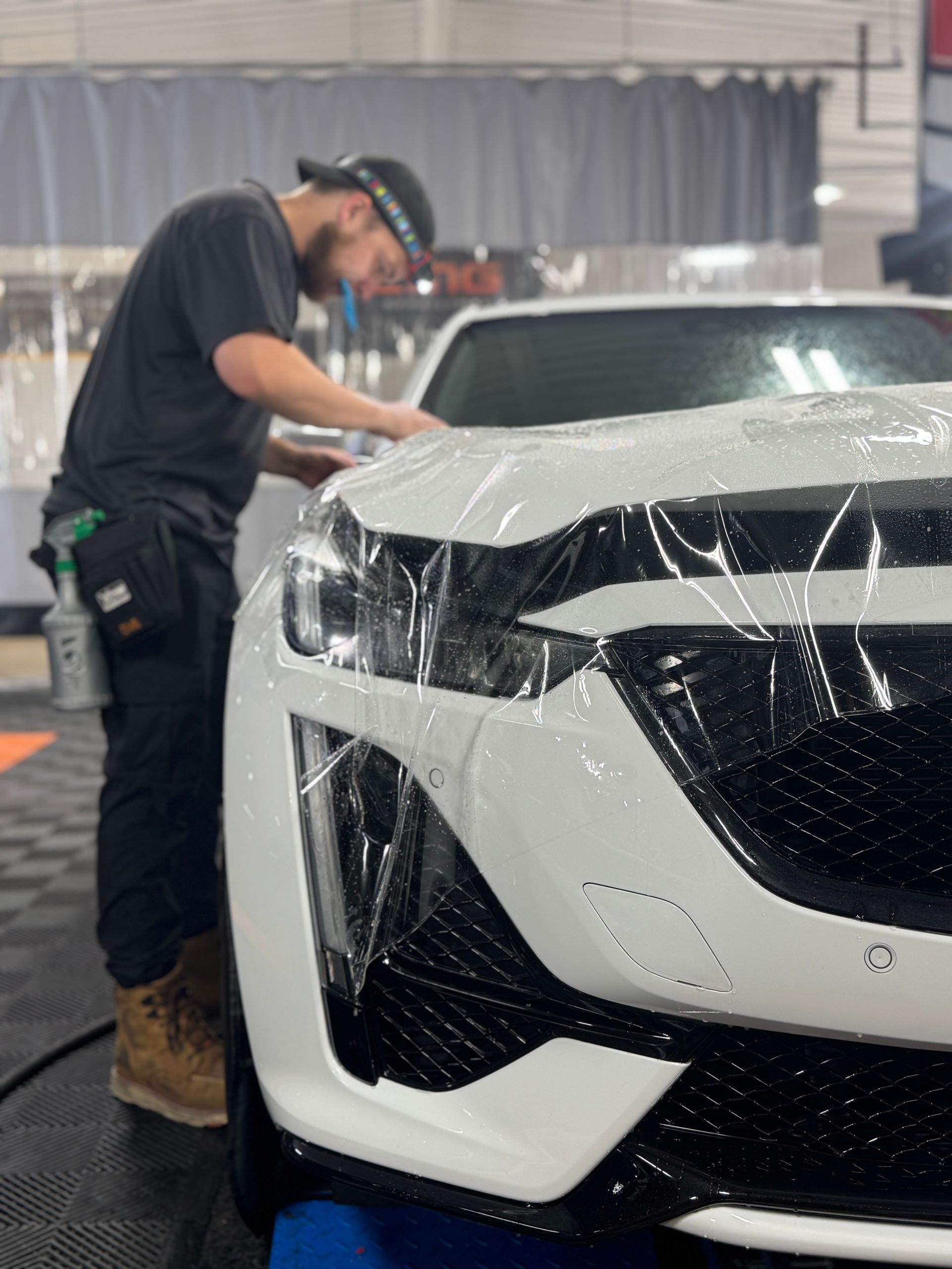 Man applying protective film to the front of a white car. Indoors, focused.