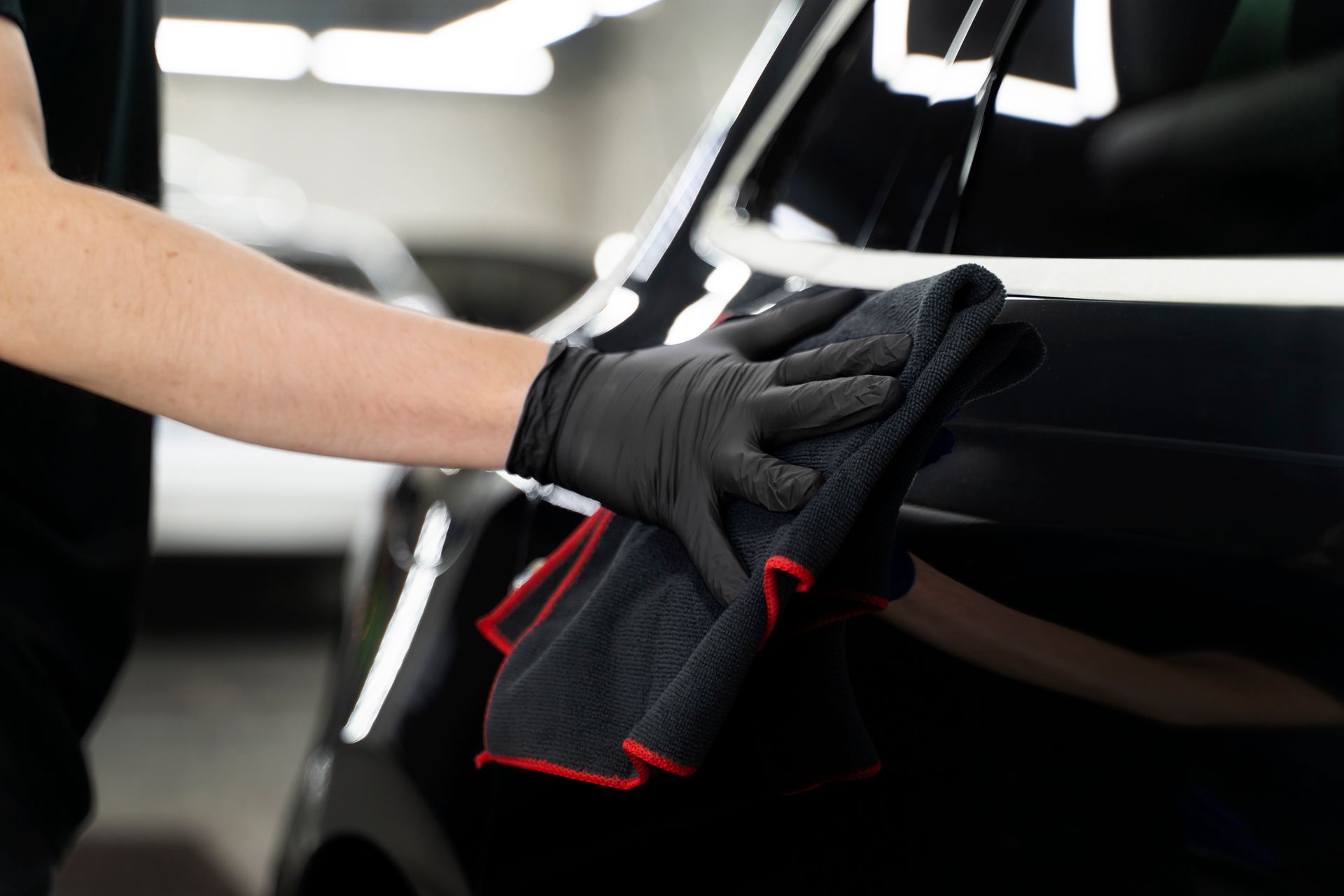 Person in black gloves wiping a shiny black car with a microfiber cloth.