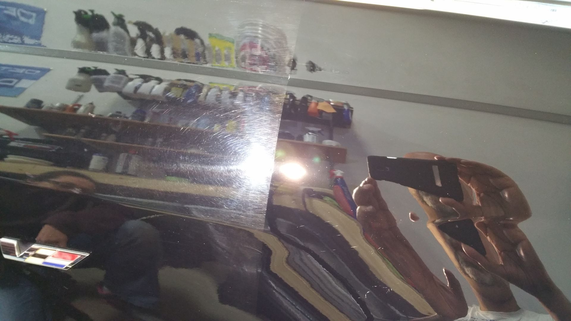 Shiny black car surface, half polished, reflecting objects in a brightly lit room.