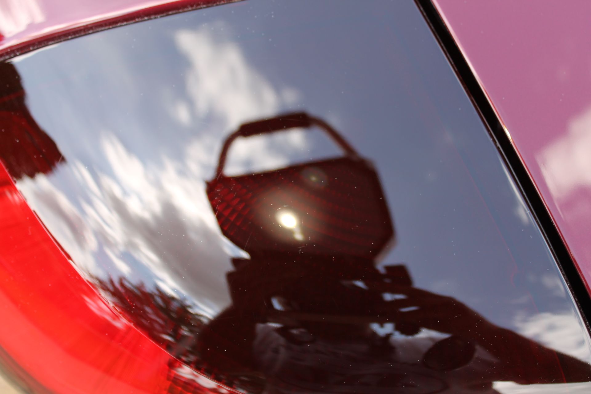 Reflection in car window shows a camera and photographer. The sky is reflected, and the car is red.