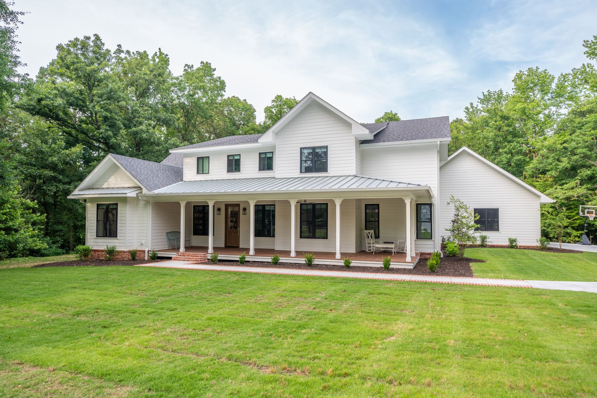 A large, two-story white farmhouse with a metal-roofed front porch, surrounded by green lawns and mature trees.