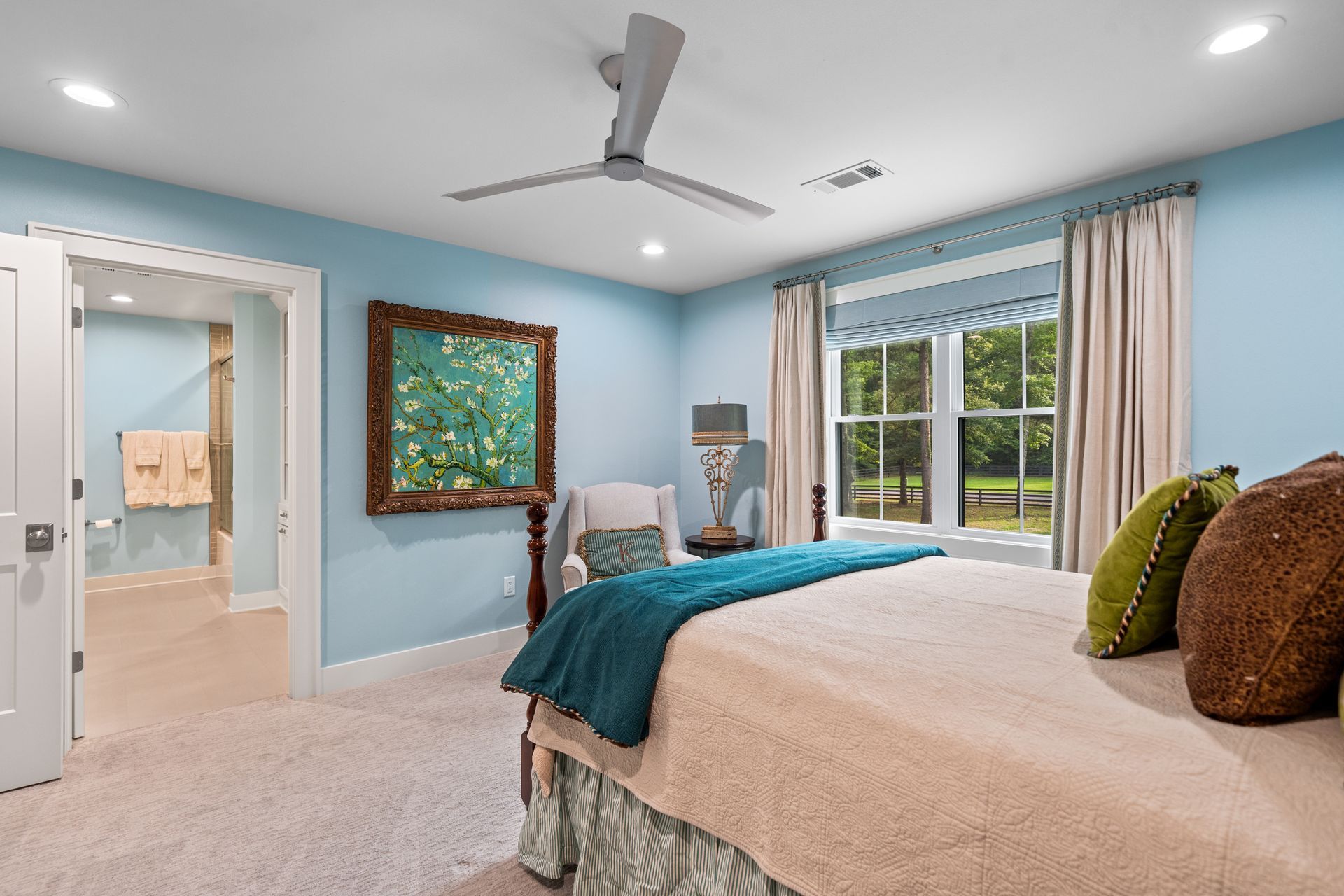 A light blue bedroom with a bed, a decorative wall painting, and an open doorway leading to a bathroom.