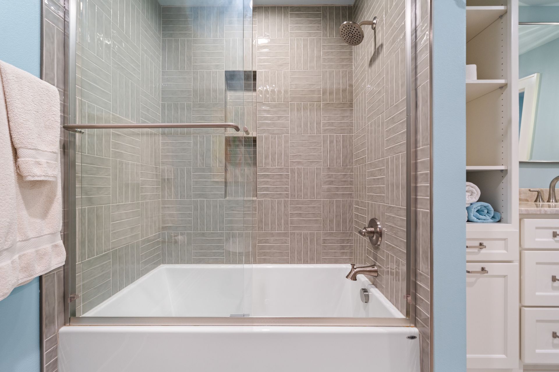 A modern bathroom featuring a white bathtub, a sliding glass door, and patterned beige tile walls.