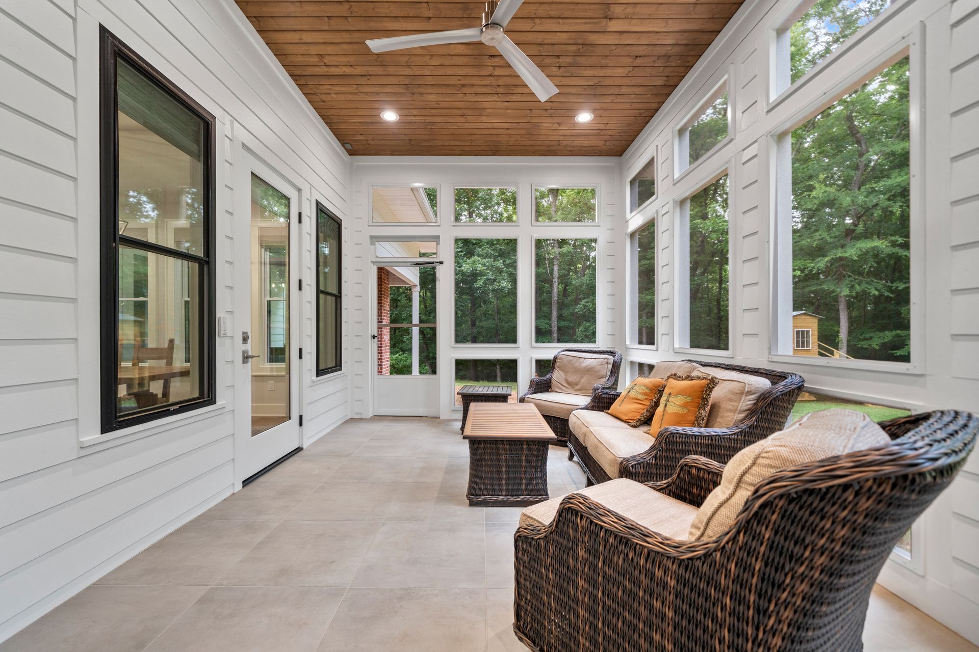A screened-in porch with white shiplap walls, a wood-paneled ceiling, ceiling fan, and wicker seating furniture.