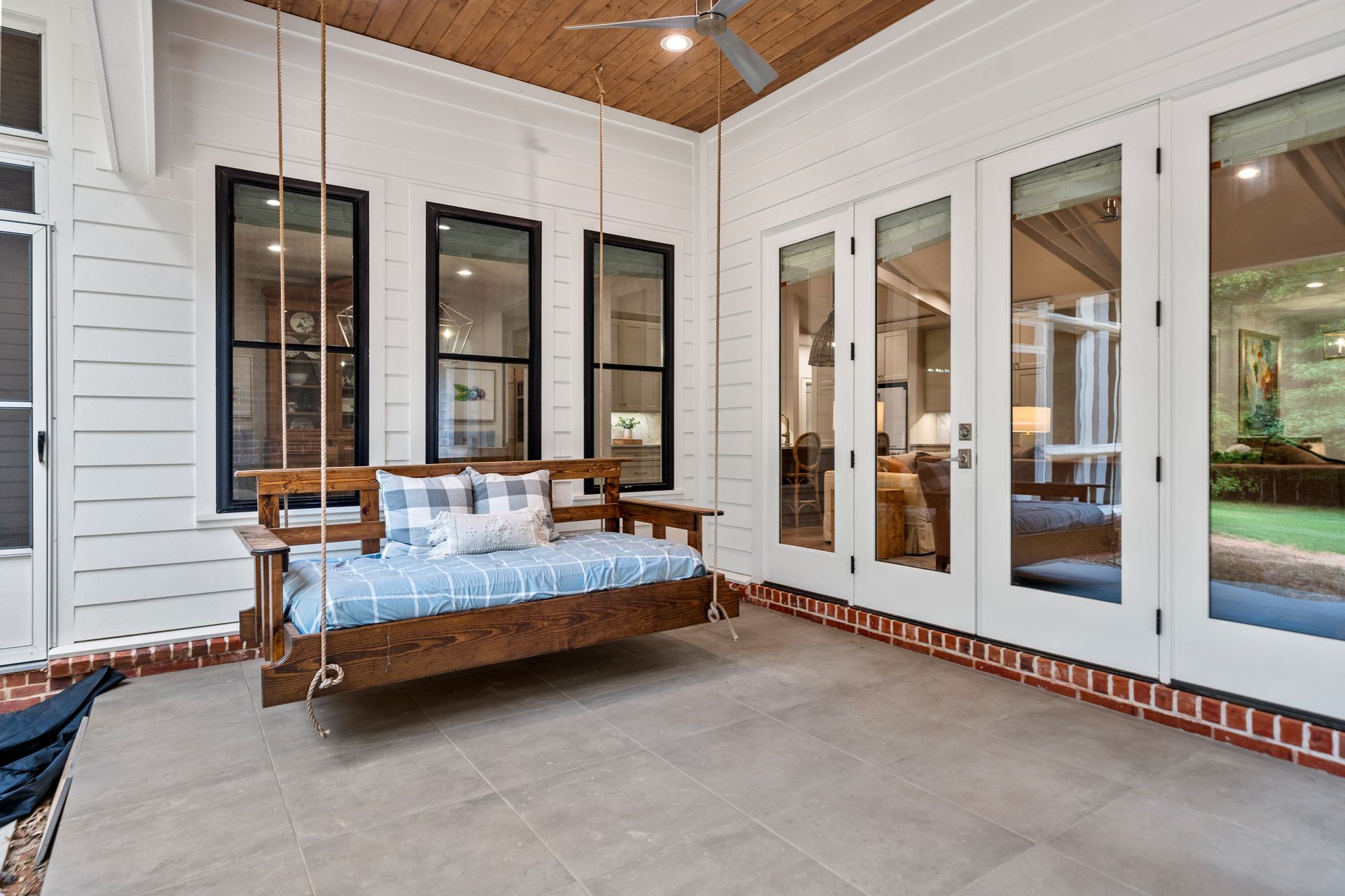 A covered porch featuring a wooden porch swing with blue plaid cushions, tile flooring, and glass doors to the interior.