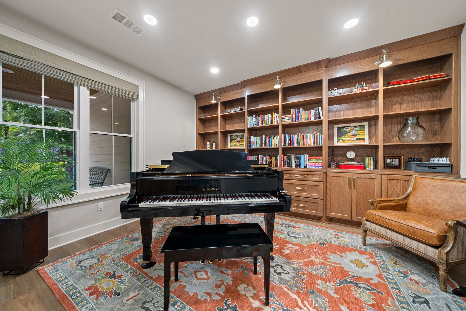 A black grand piano with a bench sits on an orange patterned rug in a home library with wall-to-wall wood bookshelves.