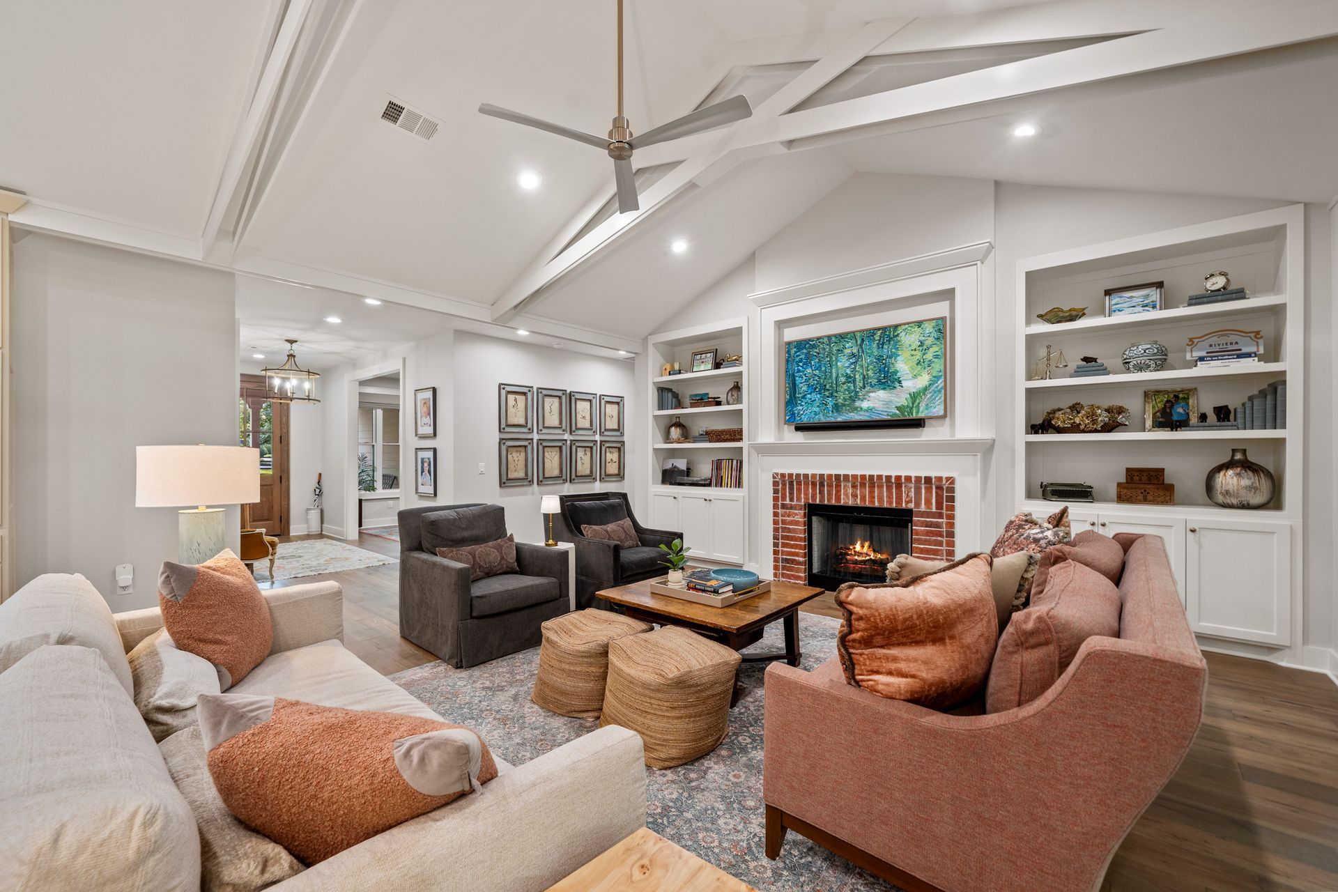 A living room featuring a vaulted ceiling, a brick fireplace with a TV, built-in shelves, and two sofas.