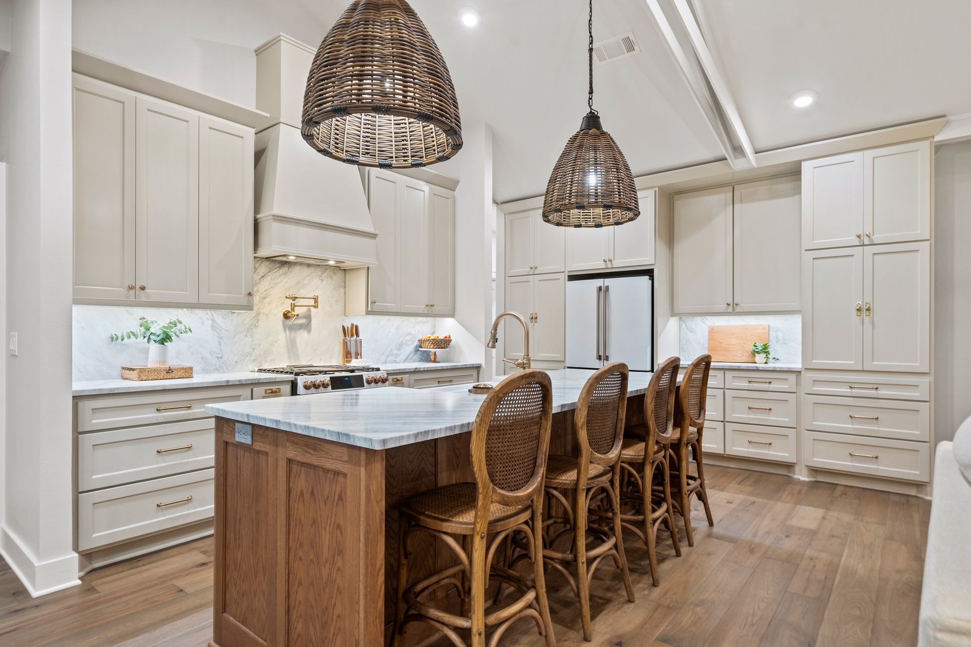 A kitchen with beige cabinets, a brown wood kitchen island with four woven stools, and two matching pendant lights above.