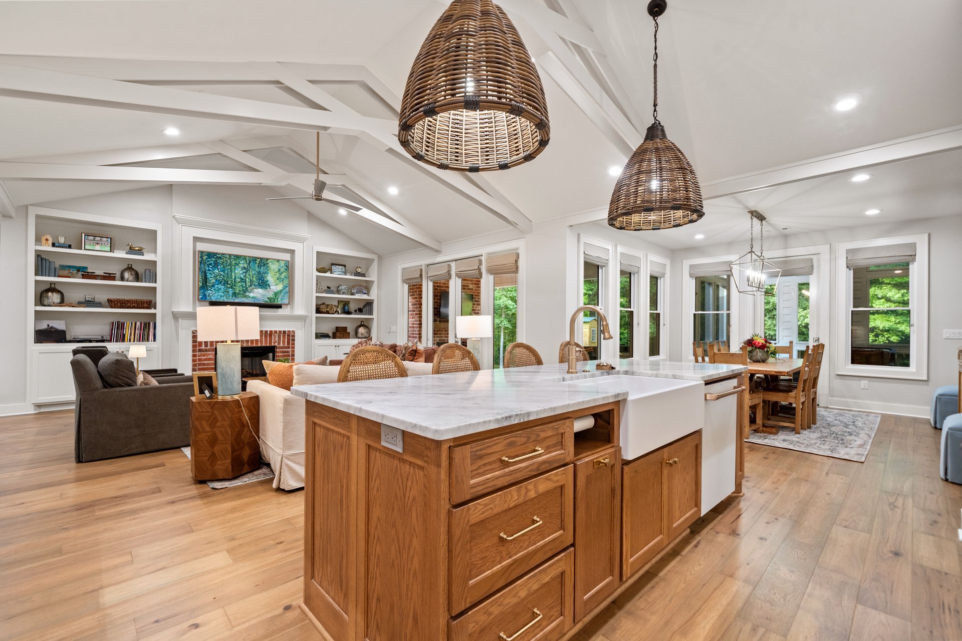 A bright, open-concept kitchen and living area featuring a wooden island with marble countertops and two wicker pendants.