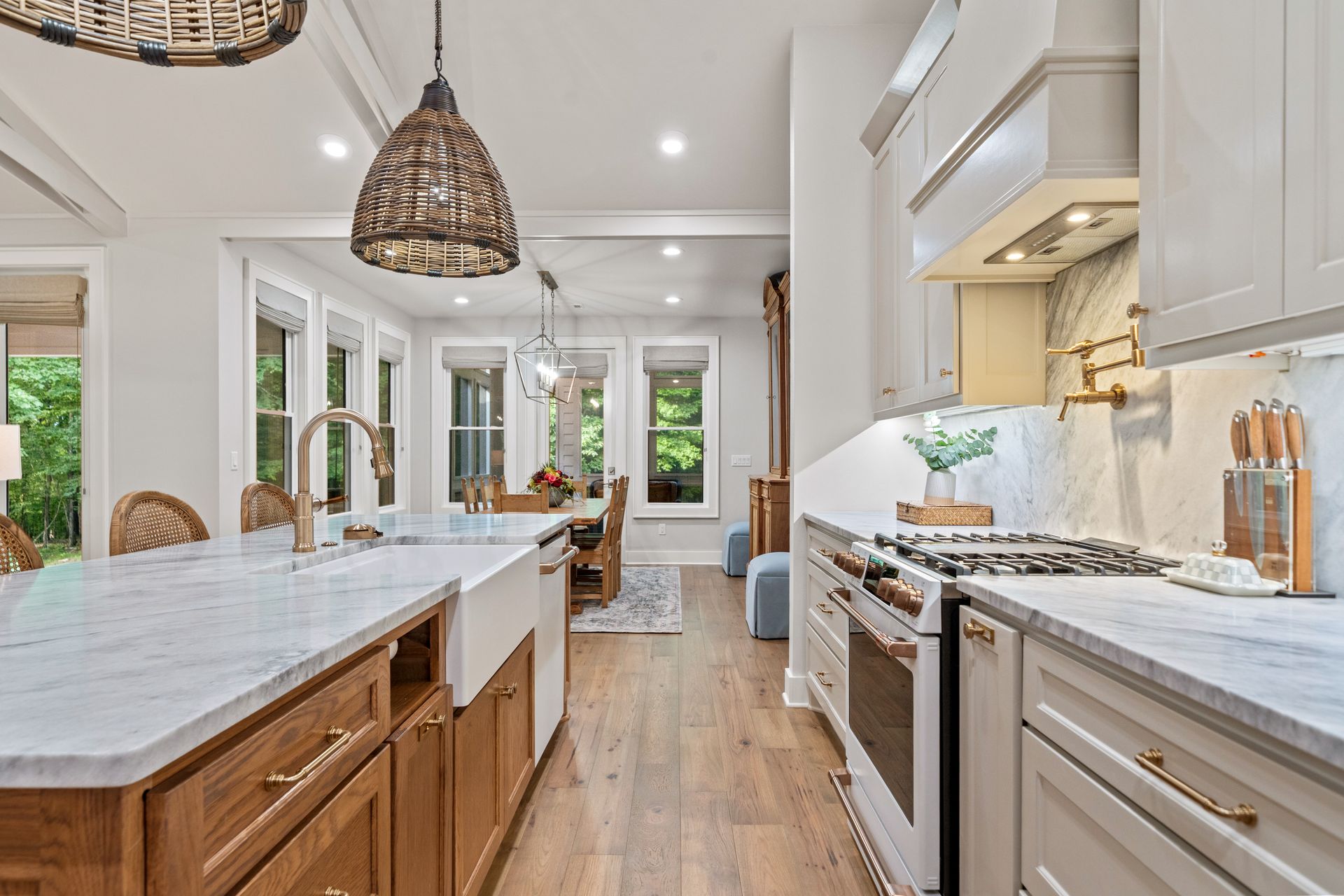 Modern kitchen with white cabinets, marble countertops, light wood base cabinets, and woven pendant lights.