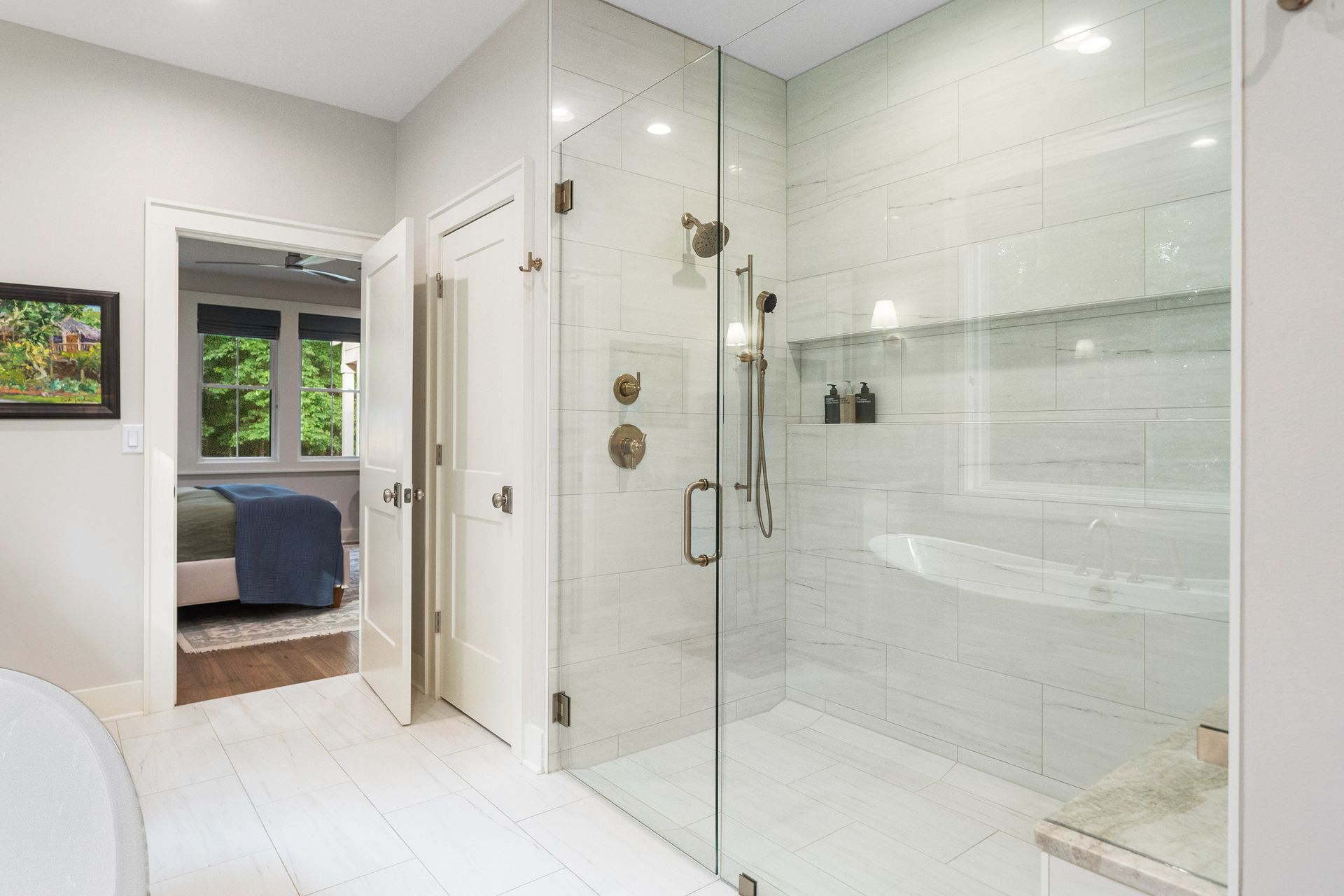 A modern bathroom featuring a glass-enclosed shower with white subway tiles, adjacent to an open door leading to a bedroom.
