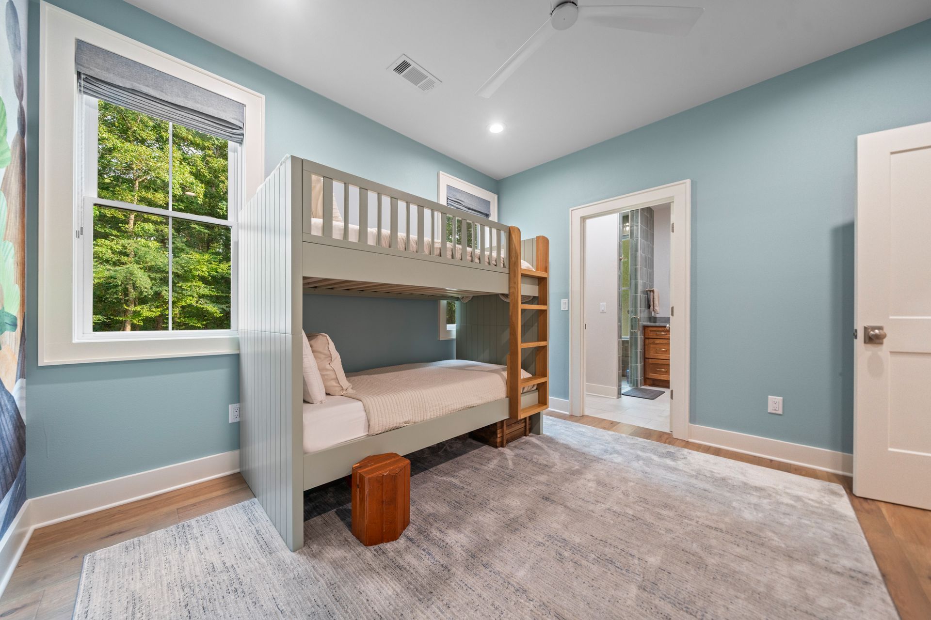 A gray bunk bed with white bedding sits in a room with light blue walls, a white rug, and an open doorway to a bathroom.