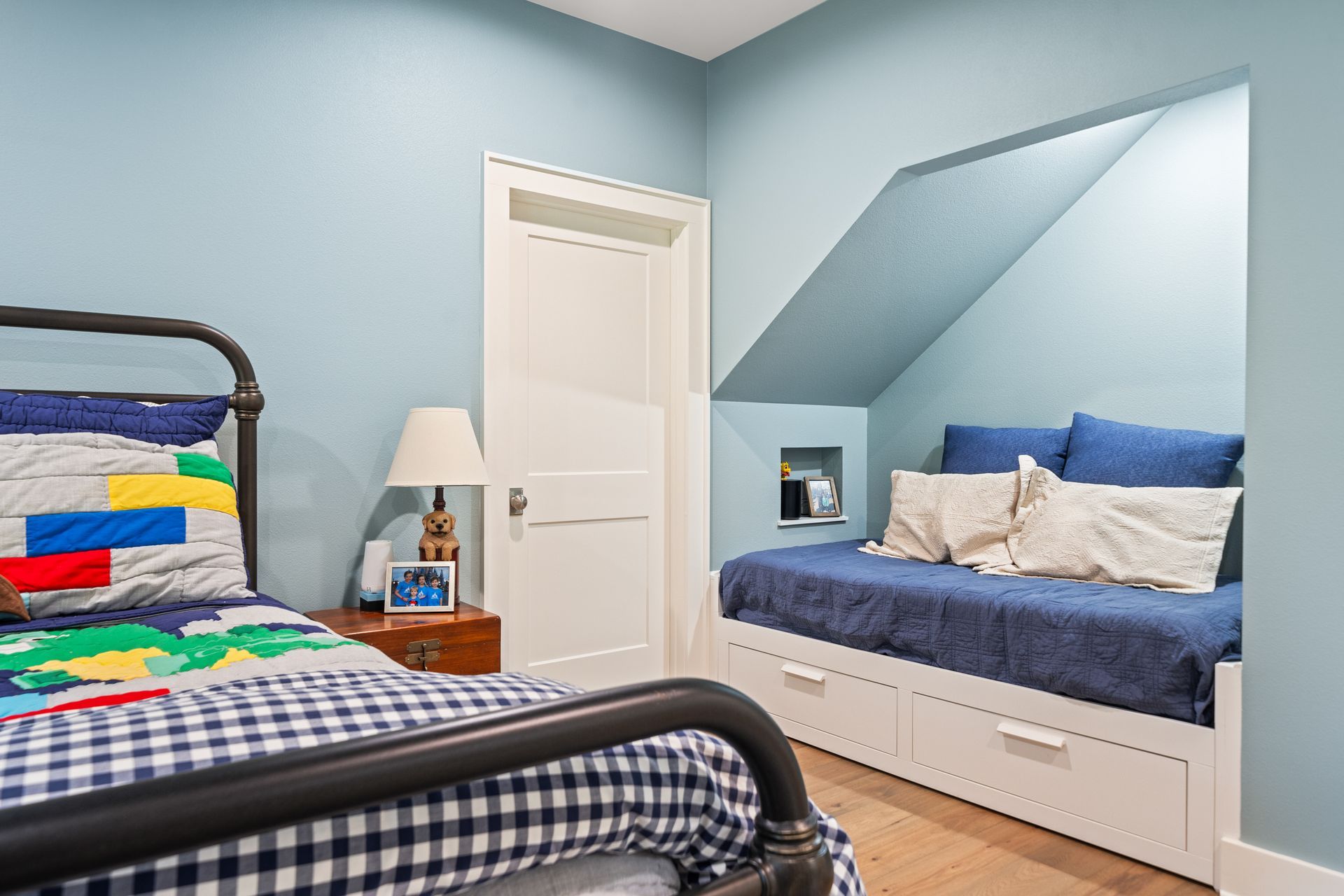A bedroom with blue walls, a metal frame bed with patterned bedding, and a built-in daybed tucked into an alcove.
