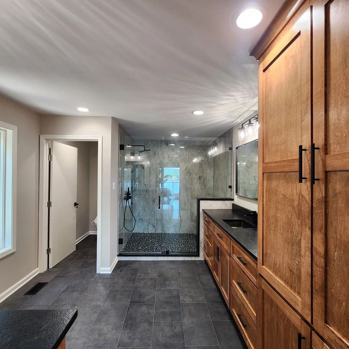 A bathroom features wood cabinets, dark granite countertops, slate tile flooring, and a glass-enclosed walk-in shower.