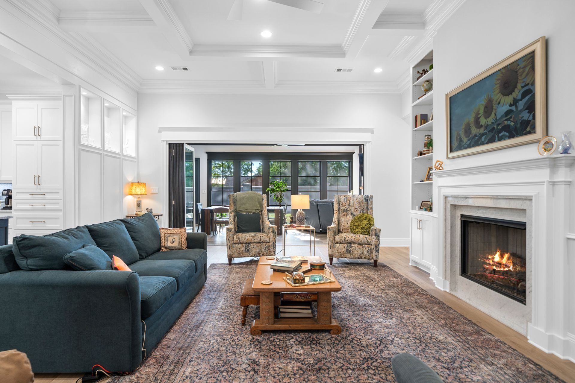 A bright living room with a navy sofa, two patterned armchairs, a coffee table, and a fireplace with art above it.