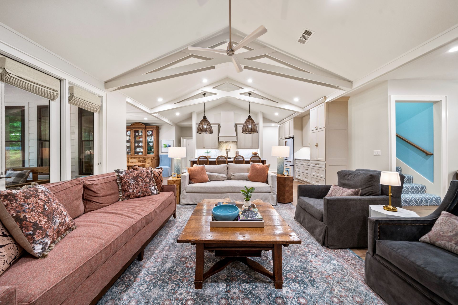 A bright bedroom with hardwood floors, a bed with blue patterned bedding, a ceiling fan, and an open doorway.