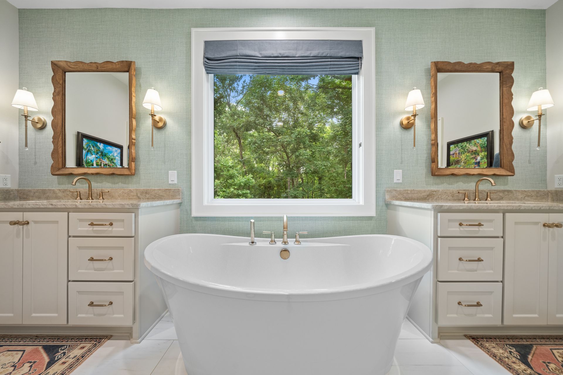A bright bathroom featuring a white vanity with a scalloped mirror, a toilet, and a bathtub with a tiled accent wall.