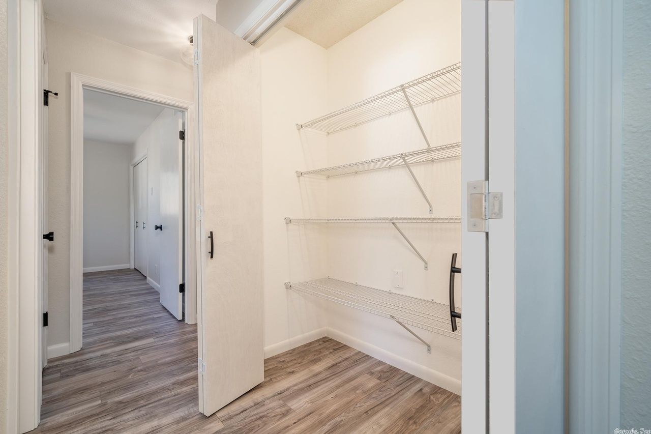 A closet with white wire shelving inside, seen from a hallway with light wood-style flooring and white doors.