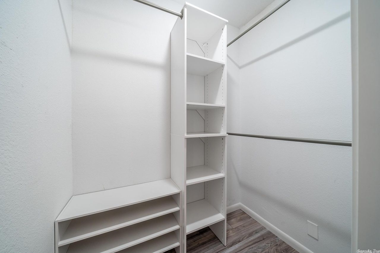 A white walk-in closet featuring shelves, a tall organizer unit, and hanging rods on a wood-look floor.