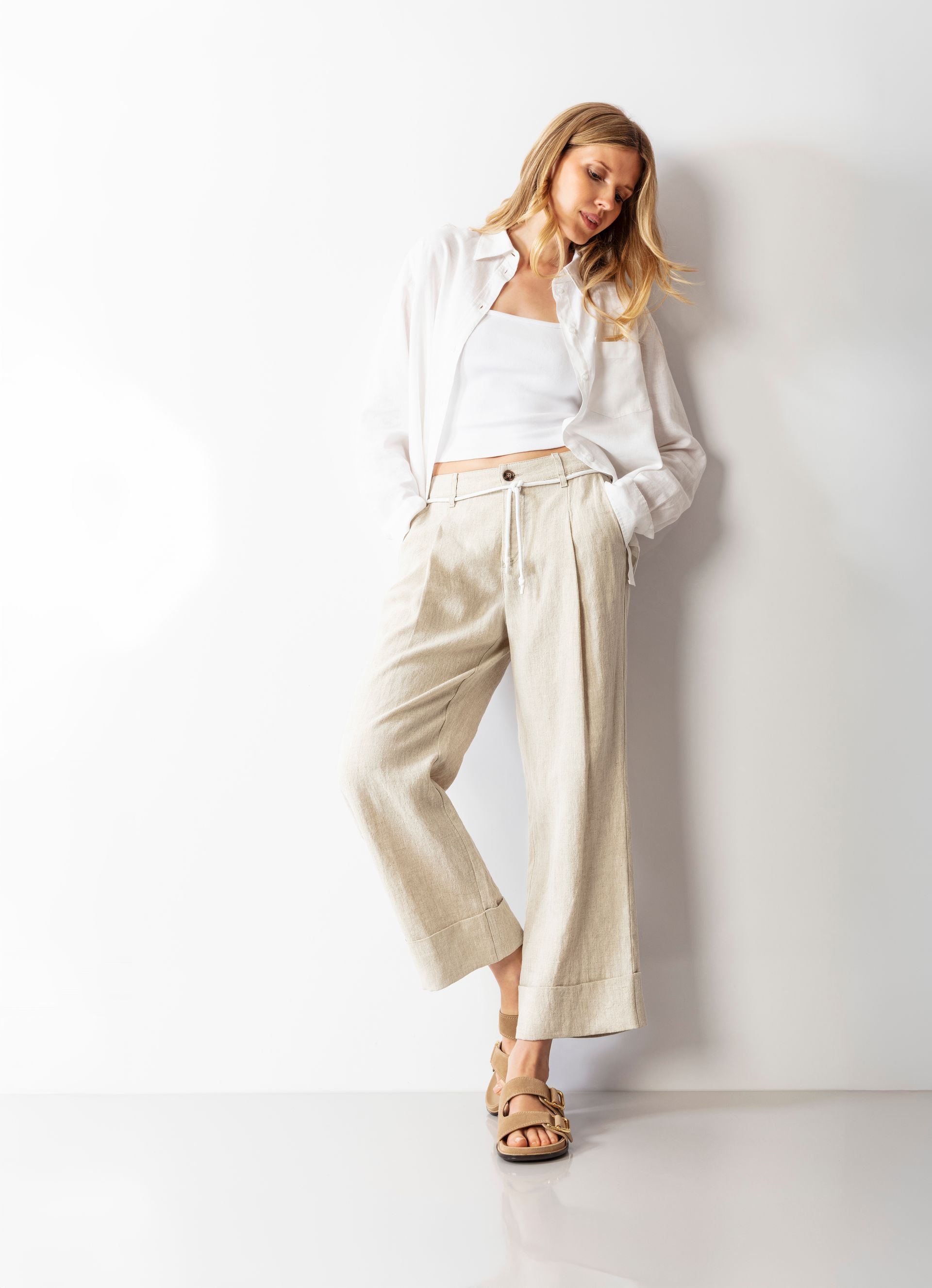 Frau in weißem Outfit lehnt an einer weißen Wand.