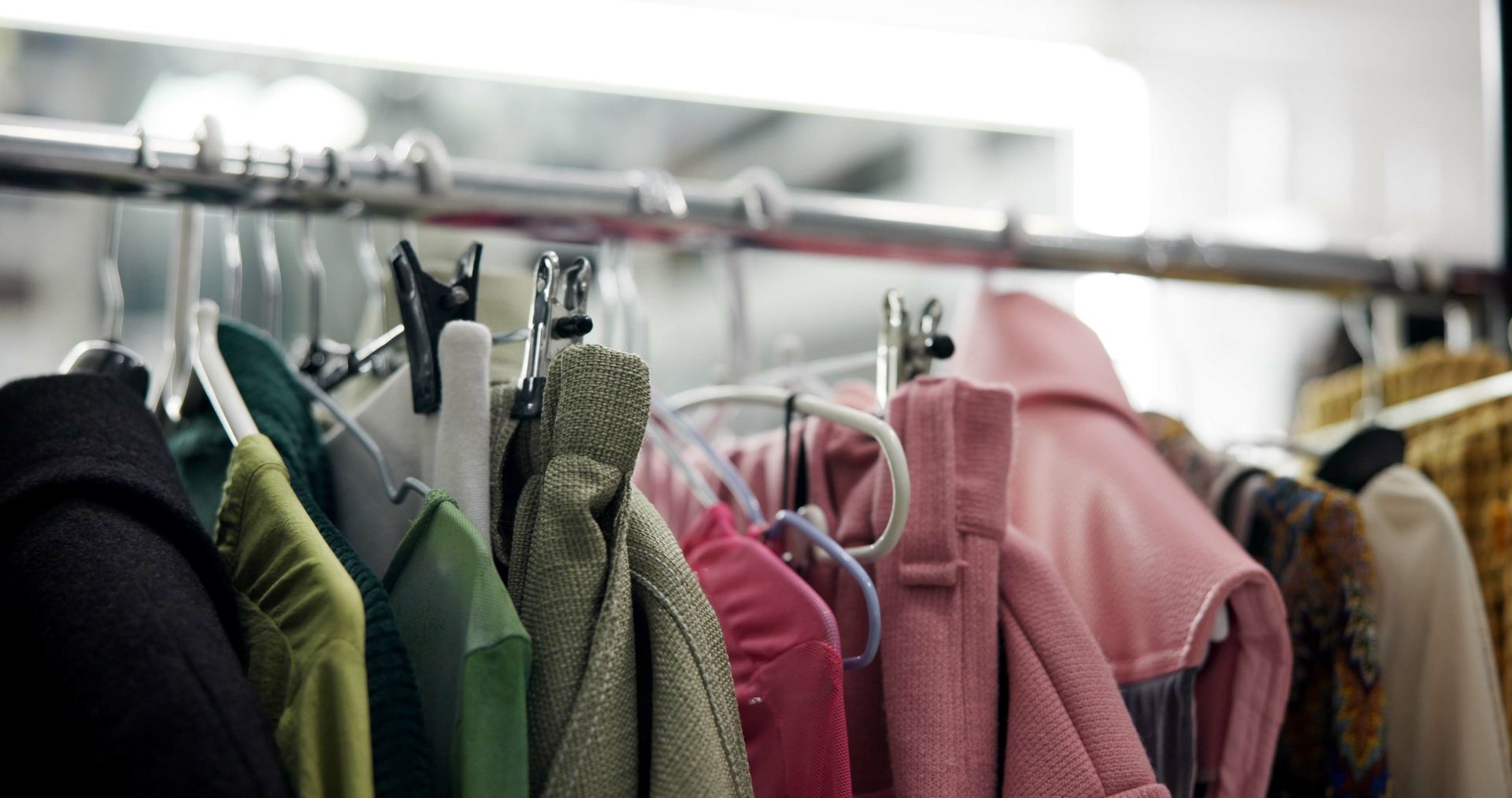 Kleiderständer mit verschiedenen Mänteln und Jacken in Grün-, Rosa- und Schwarztönen.