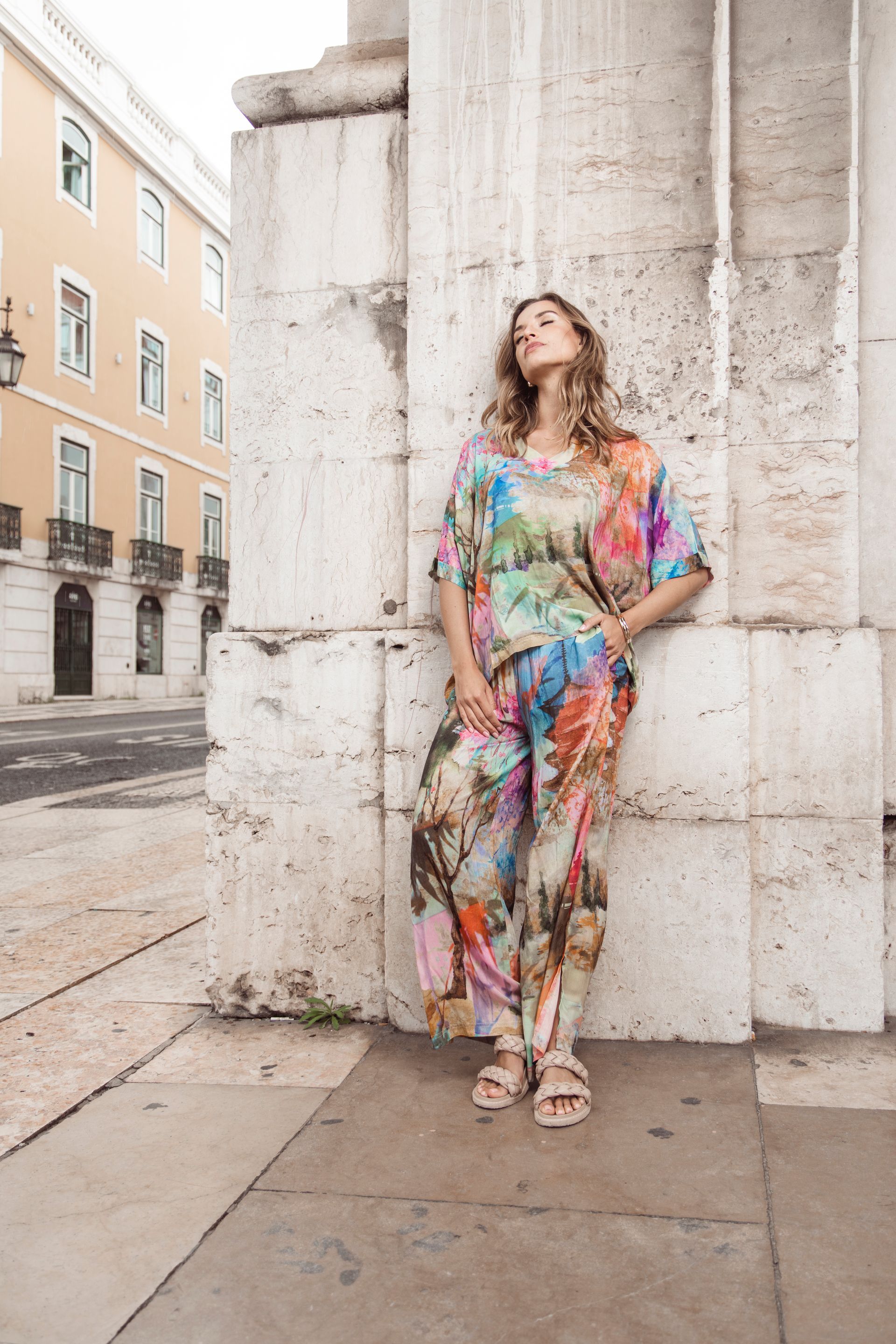 Eine Frau in farbenfroher Kleidung lehnt im Freien an einer Steinsäule.