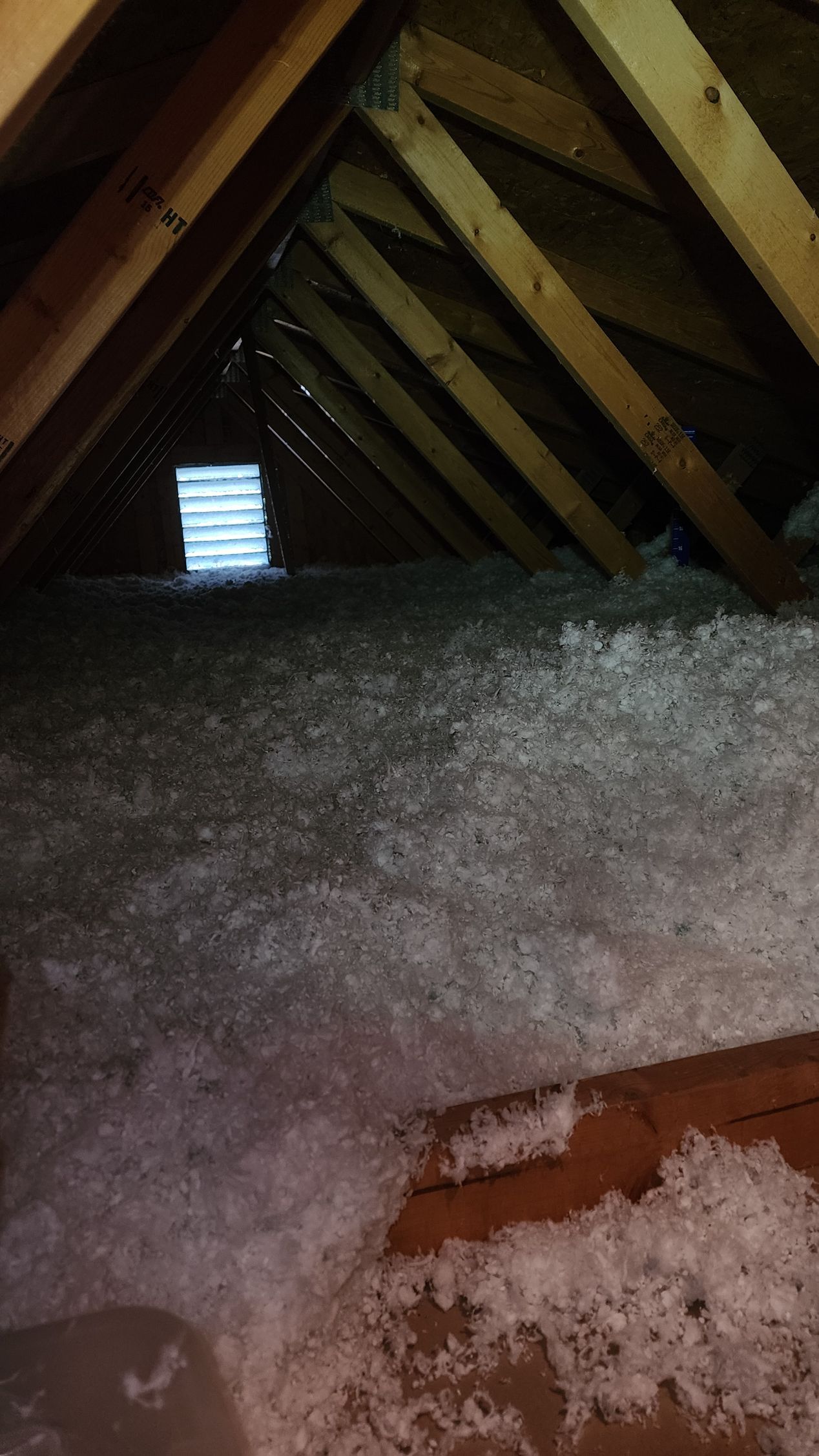 An attic filled with white insulation and a window.