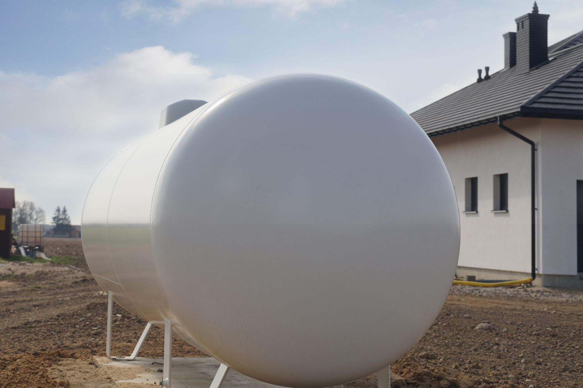 Residential home heating oil tank installed beside modern house in outdoor residential yard area.