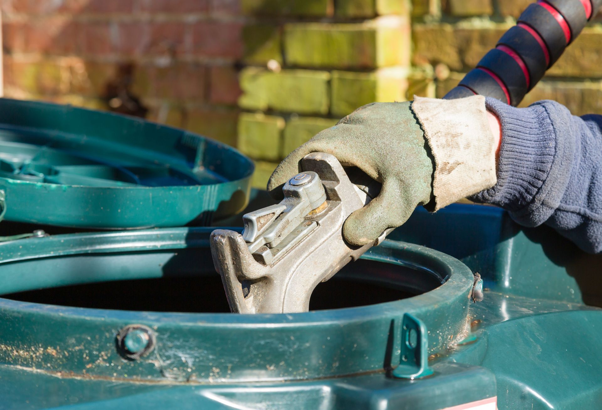 Heating oil delivery services technician filling residential oil tank with fuel nozzle outdoors.