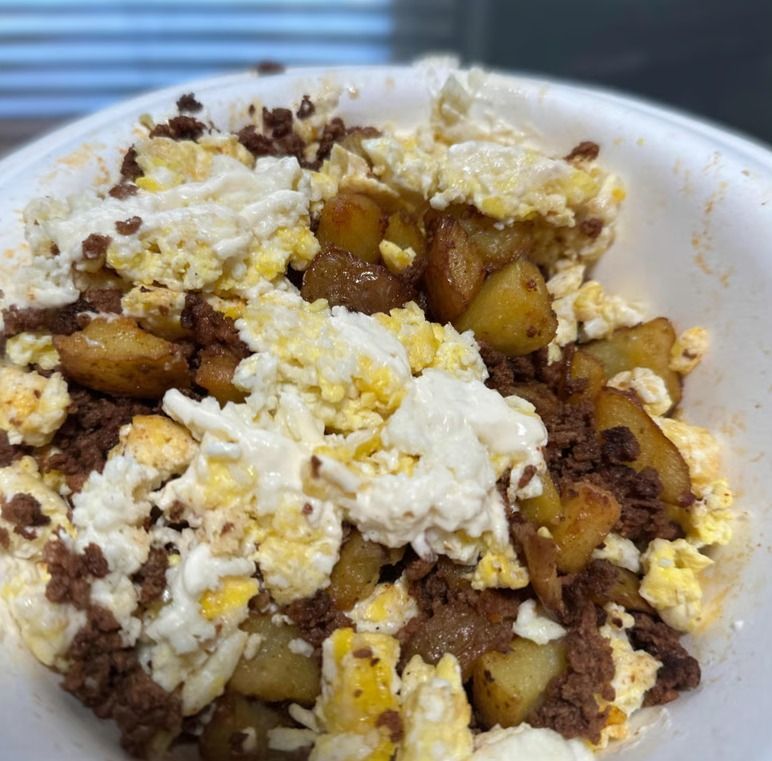 A white bowl filled with a breakfast scramble of diced potatoes, crumbled ground meat, and fluffy scrambled eggs.