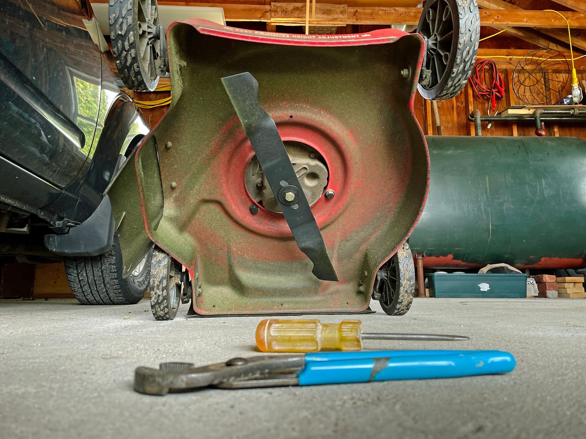 Lawnmower upside down, blade exposed, with wrench and screwdriver on ground in a garage. Lawnmower upside down, blade exposed, with wrench and screwdriver on ground in a garage.