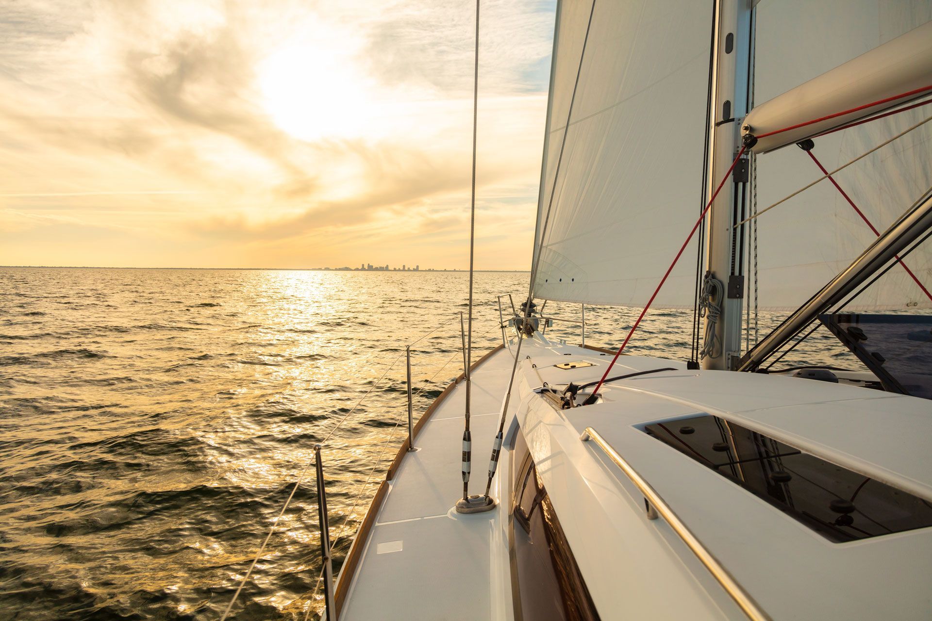 Sailboat sailing on a calm ocean at sunset; golden light reflects on the water.