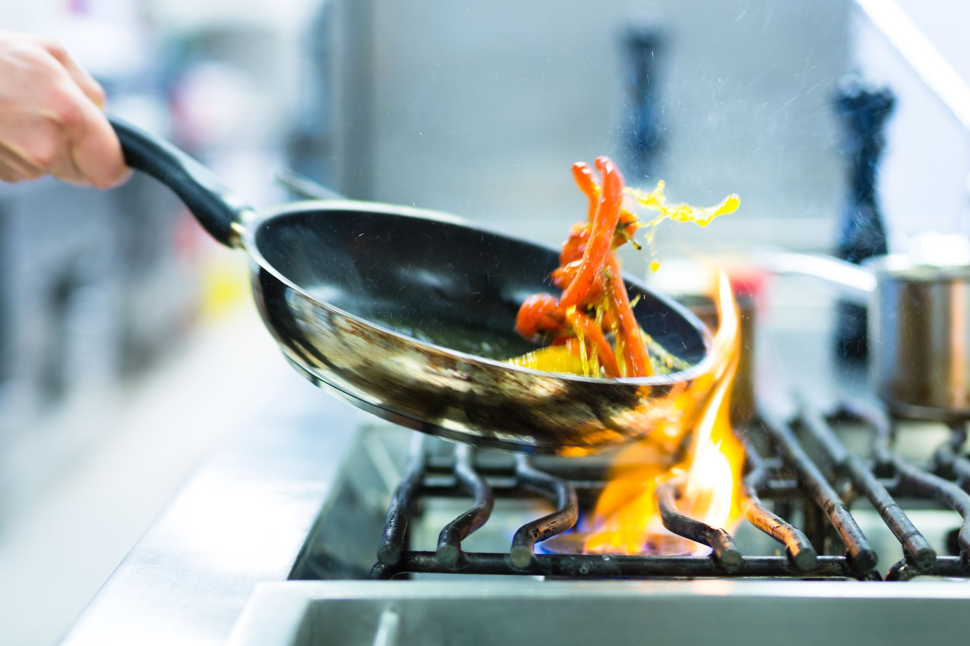Person flipping food in a flaming pan on a gas stovetop in a kitchen.